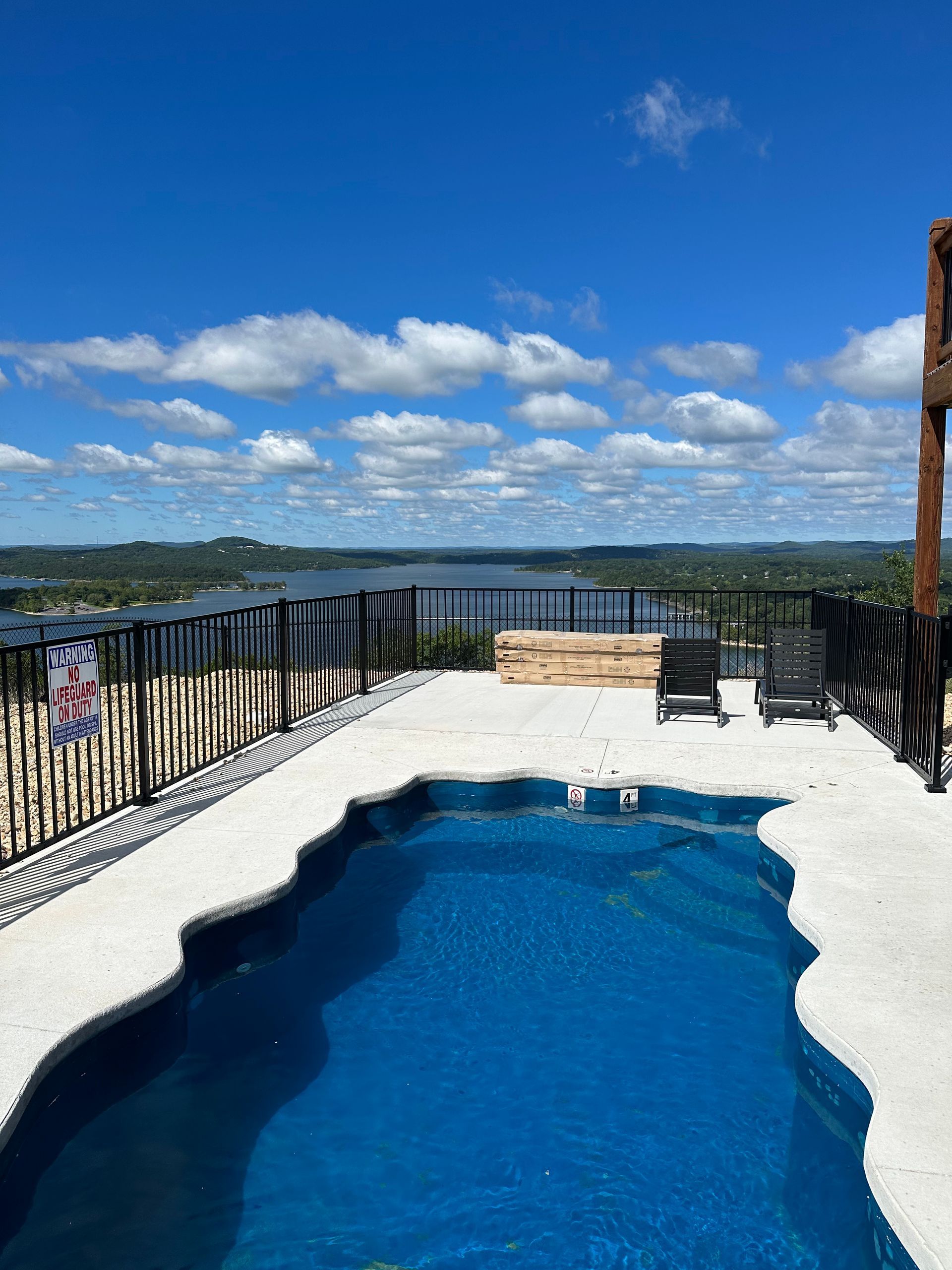 Blue pool on a rooftop terrace overlooking water and hills under a bright blue sky with clouds