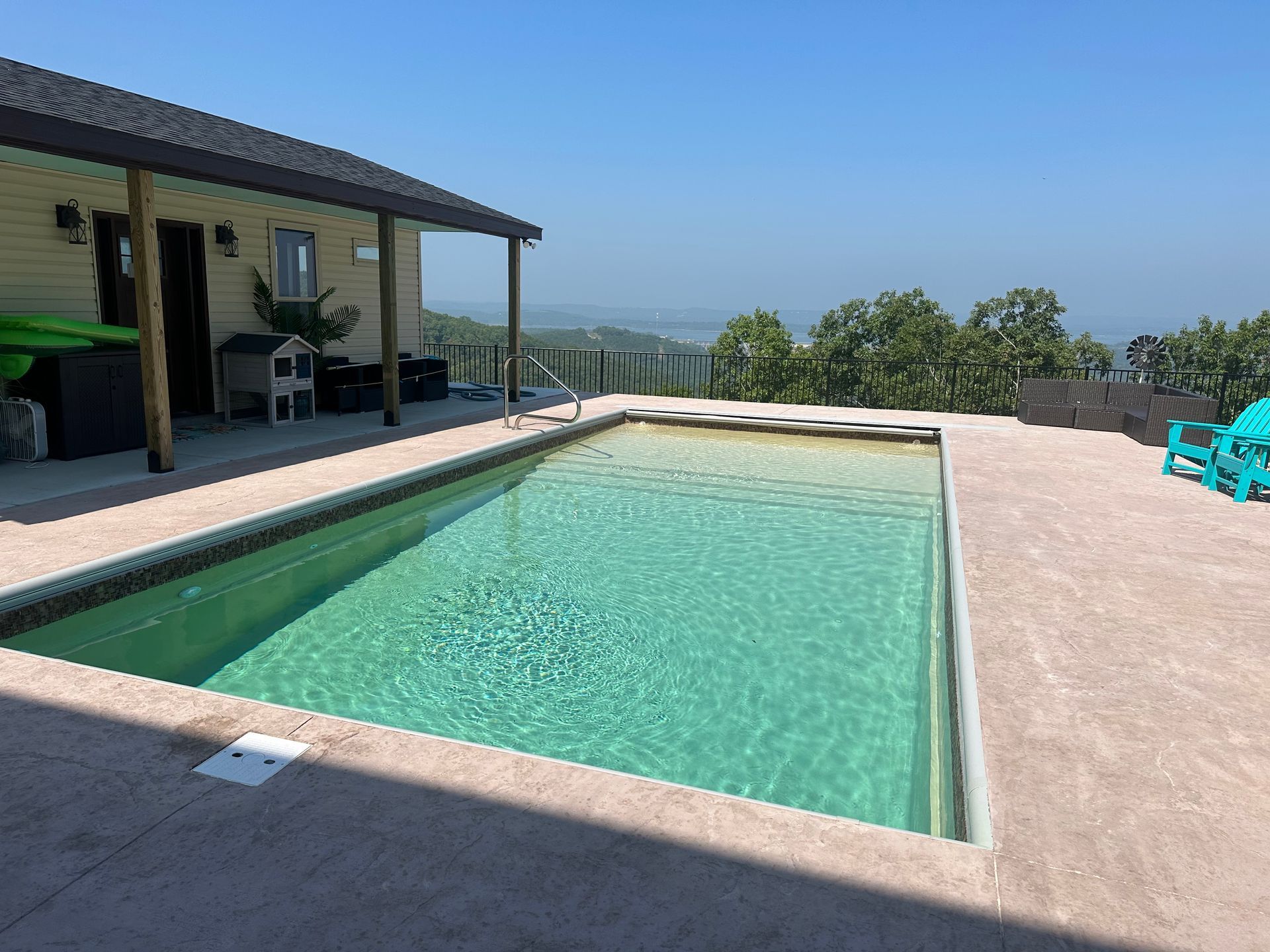Outdoor patio with a rectangular swimming pool, tiled deck, and ocean view beyond.
