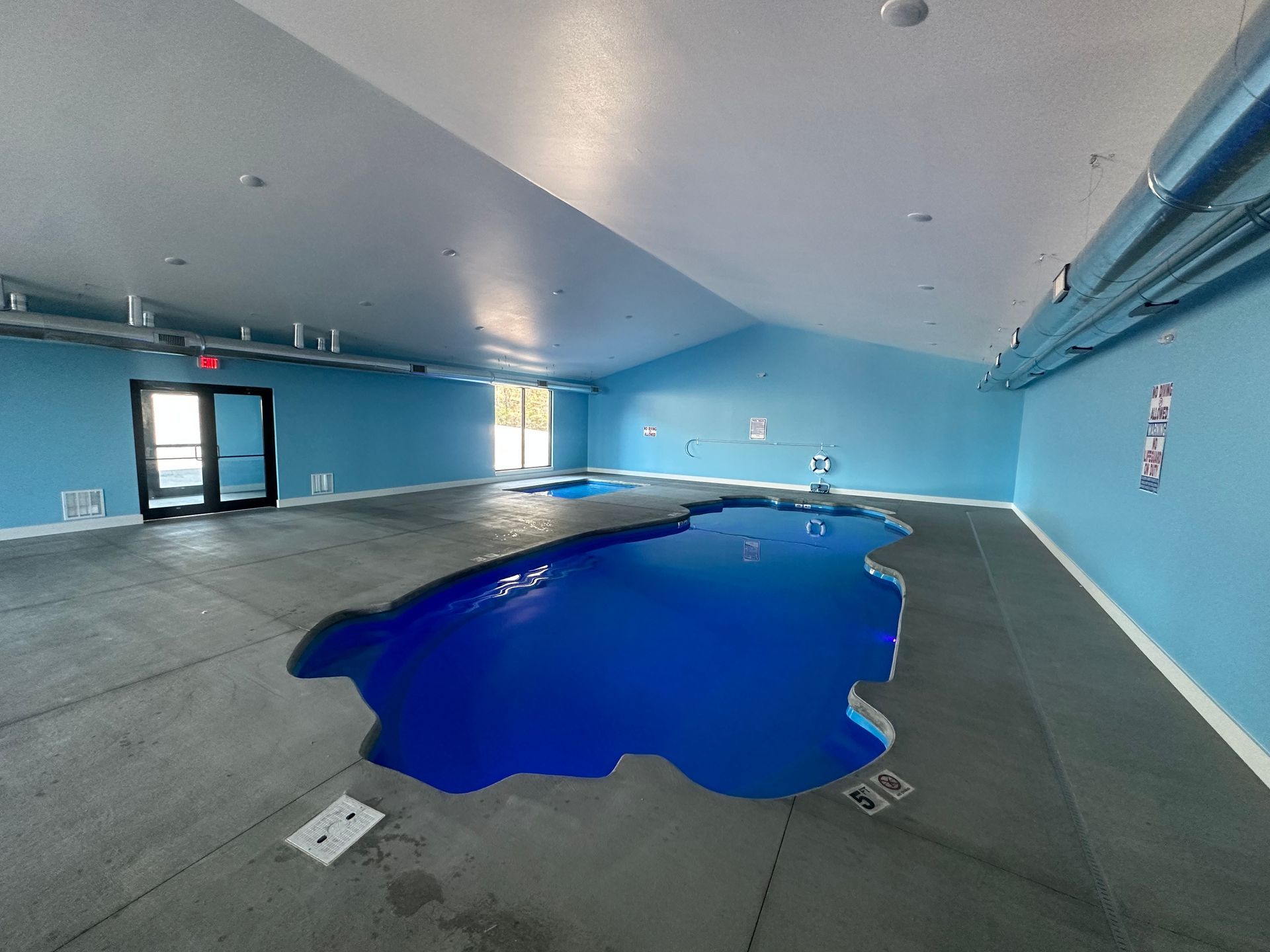 Empty indoor pool room with bright blue walls and a drained pool basin