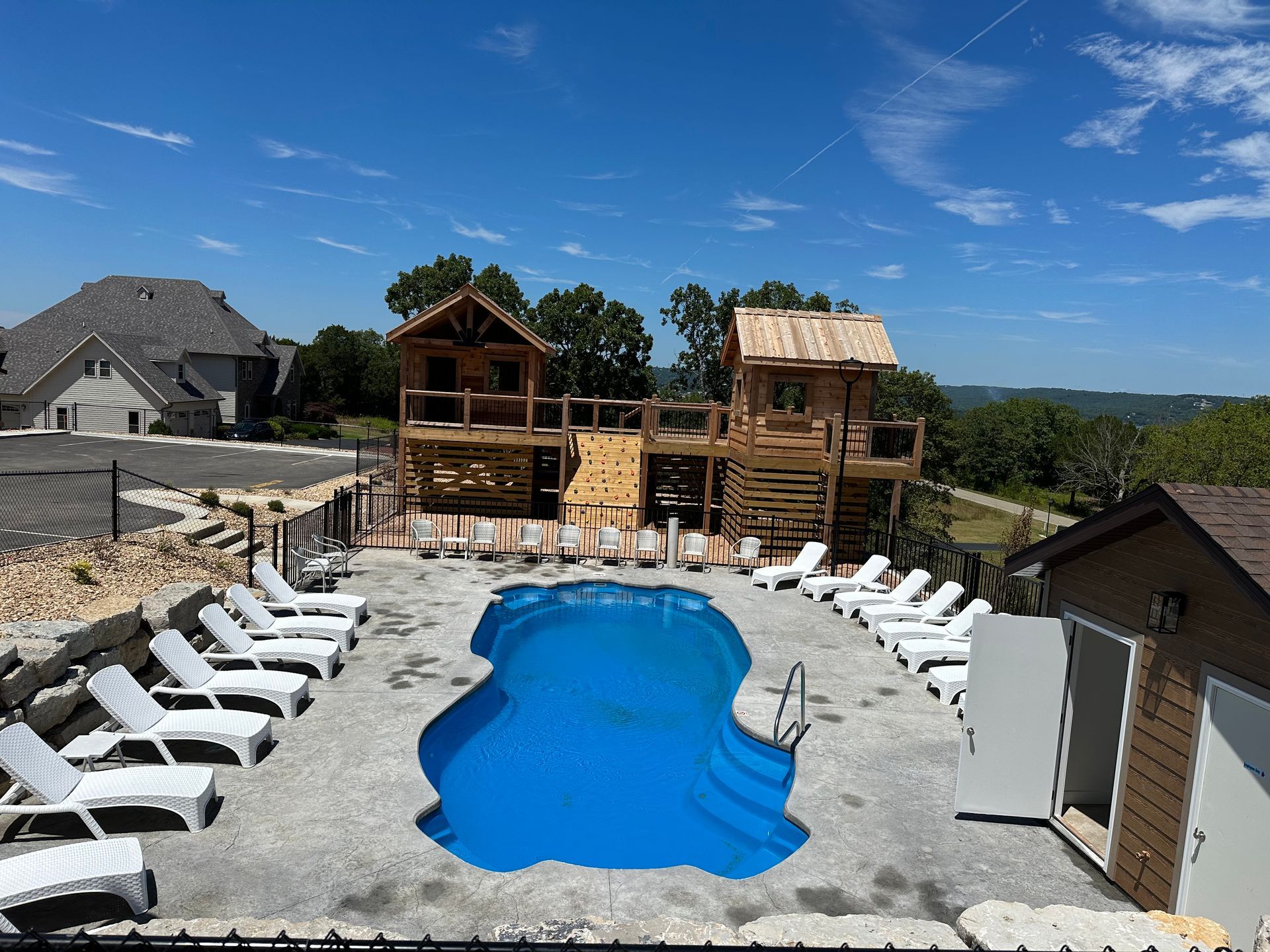 Backyard pool with white lounge chairs and wooden play structures under a blue sky