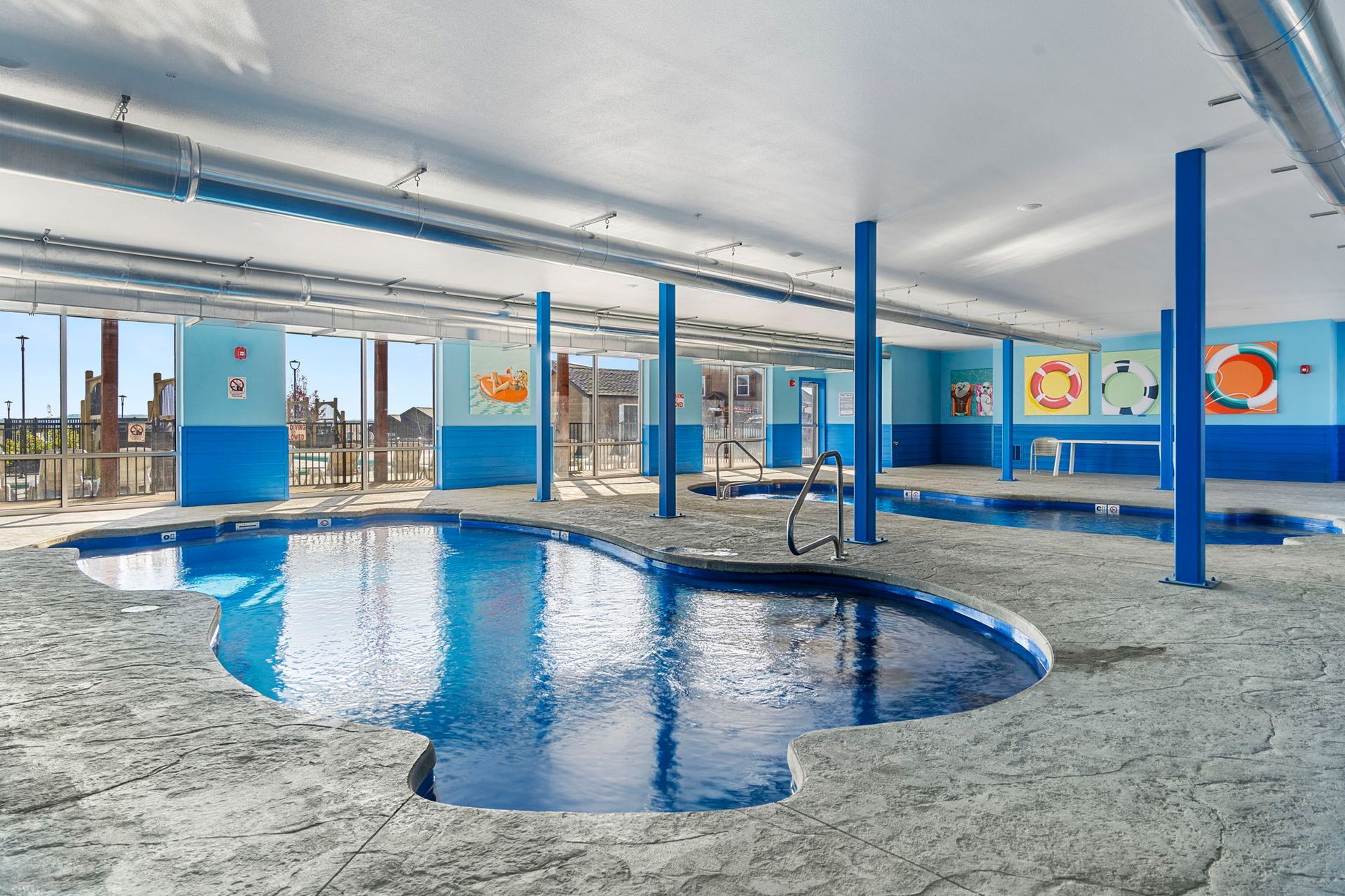 Indoor pool under construction with blue pillars, curved pool basin, and large windows.