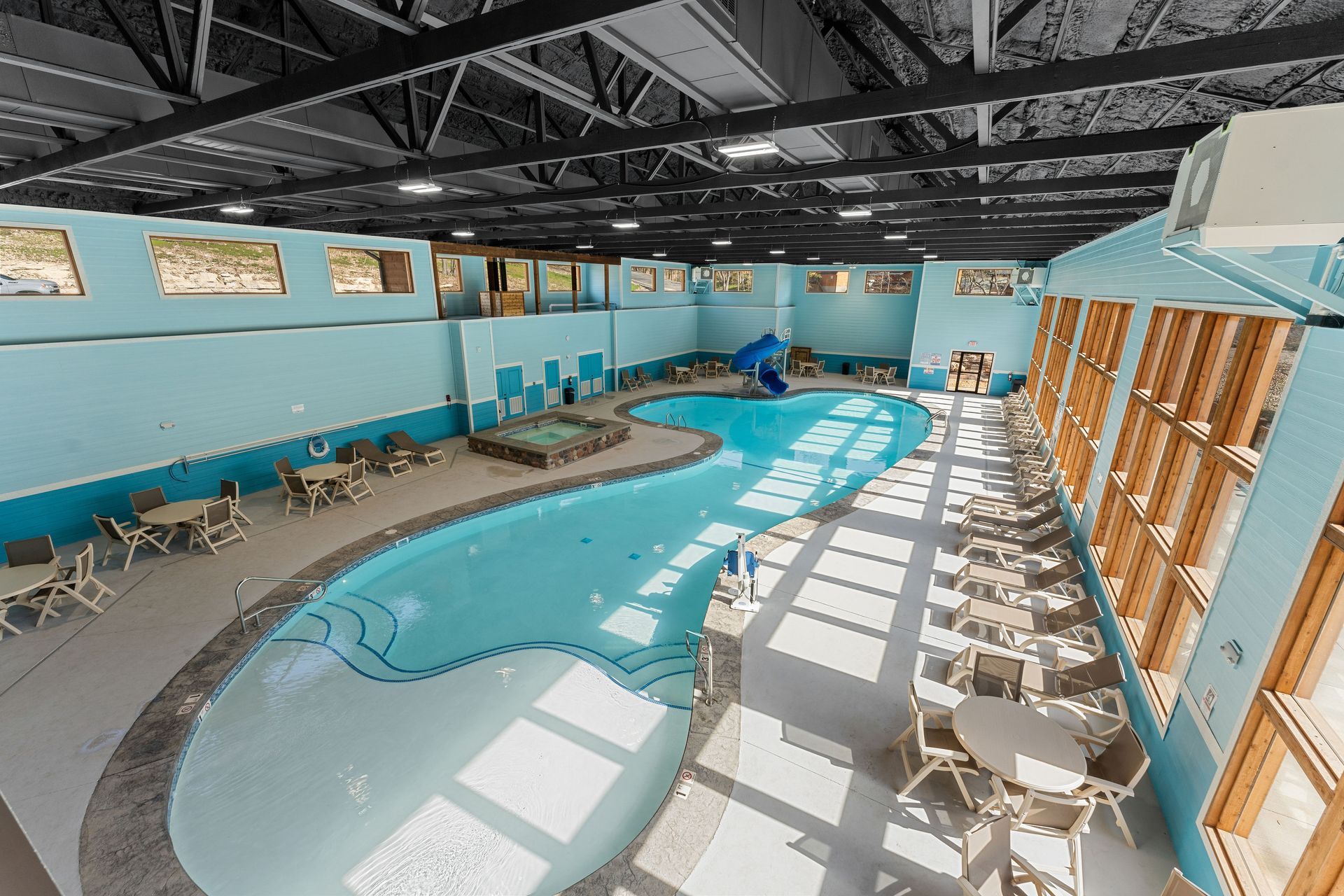Indoor swimming pool with curved blue water, lounge chairs, and sunlight through large windows