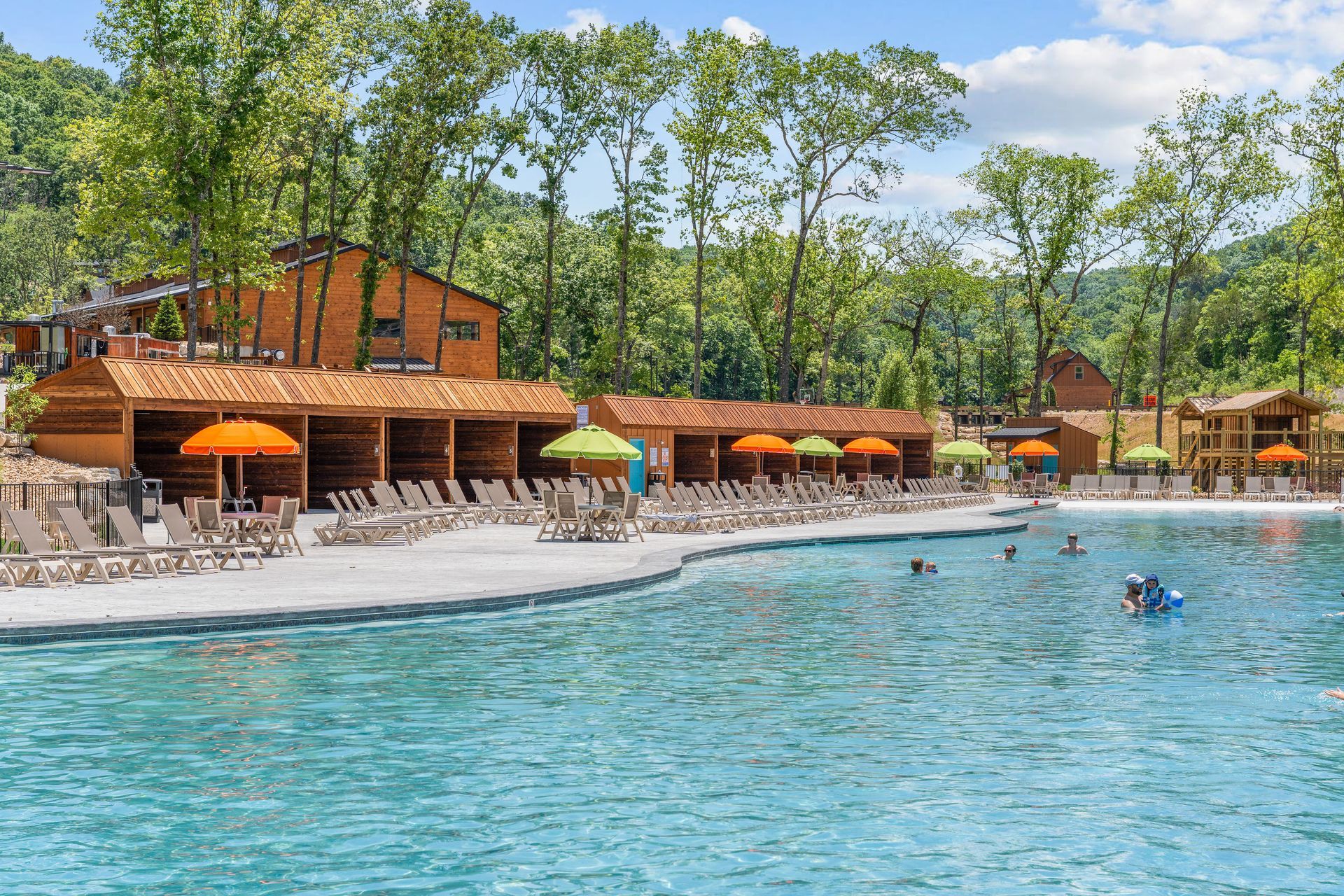 Resort pool with blue water, orange umbrellas, and a wooden lodge surrounded by trees