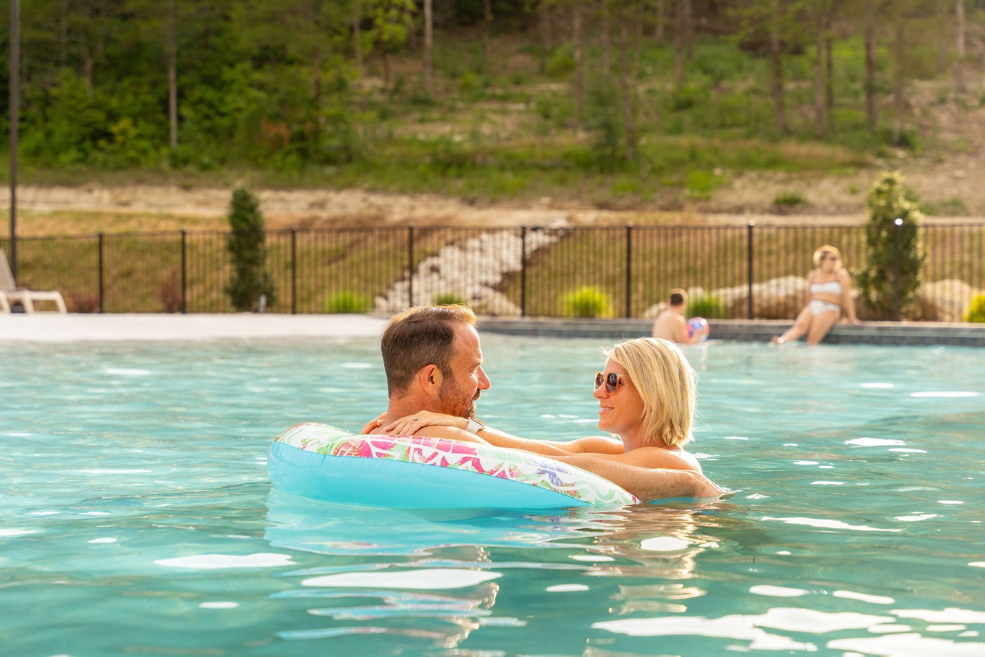 Couple relaxing in a turquoise pool, facing each other near the water’s edge.