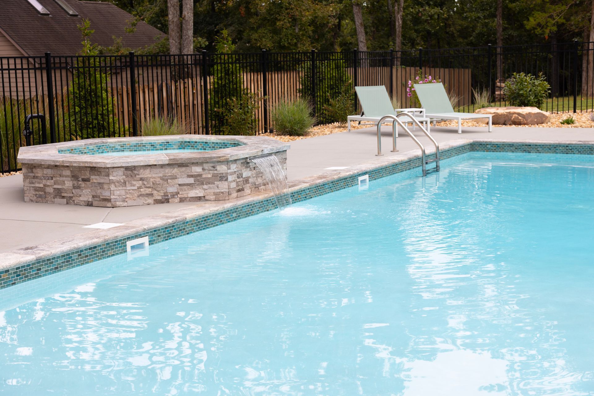 Backyard swimming pool with a stone hot tub and lounge chairs beside it