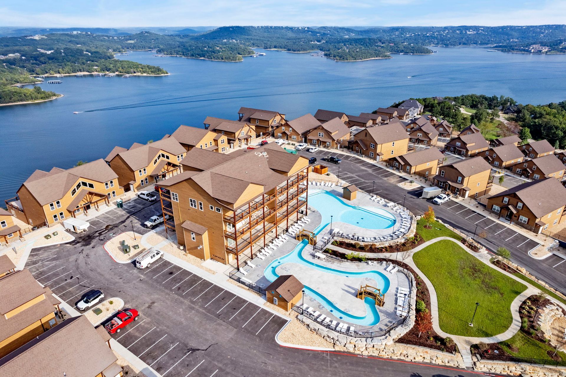 Aerial view of a waterfront resort with two outdoor pools, tan buildings, and a lake in the background