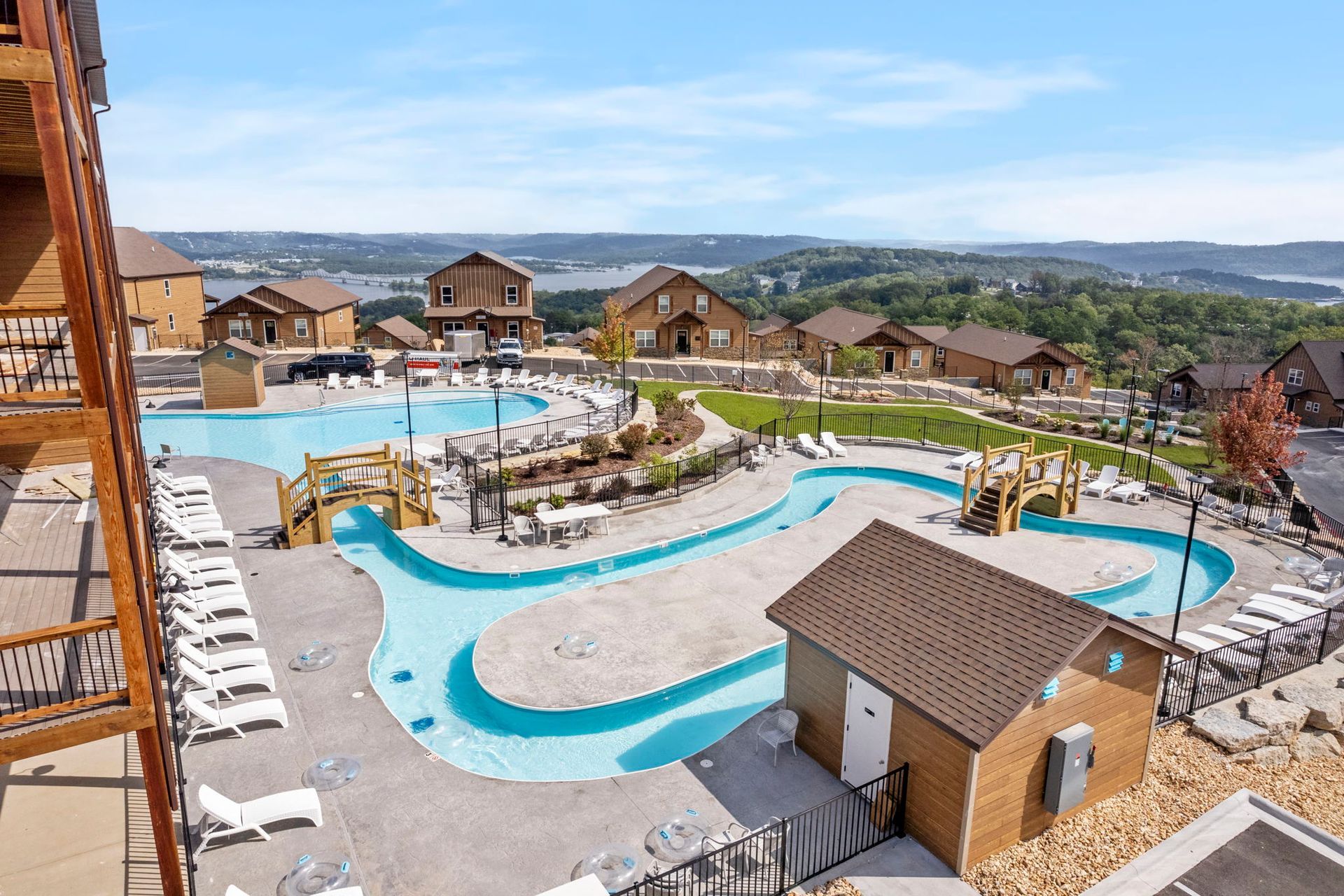 Resort pool with winding lazy river, lounge chairs, and cabins overlooking a coastal landscape