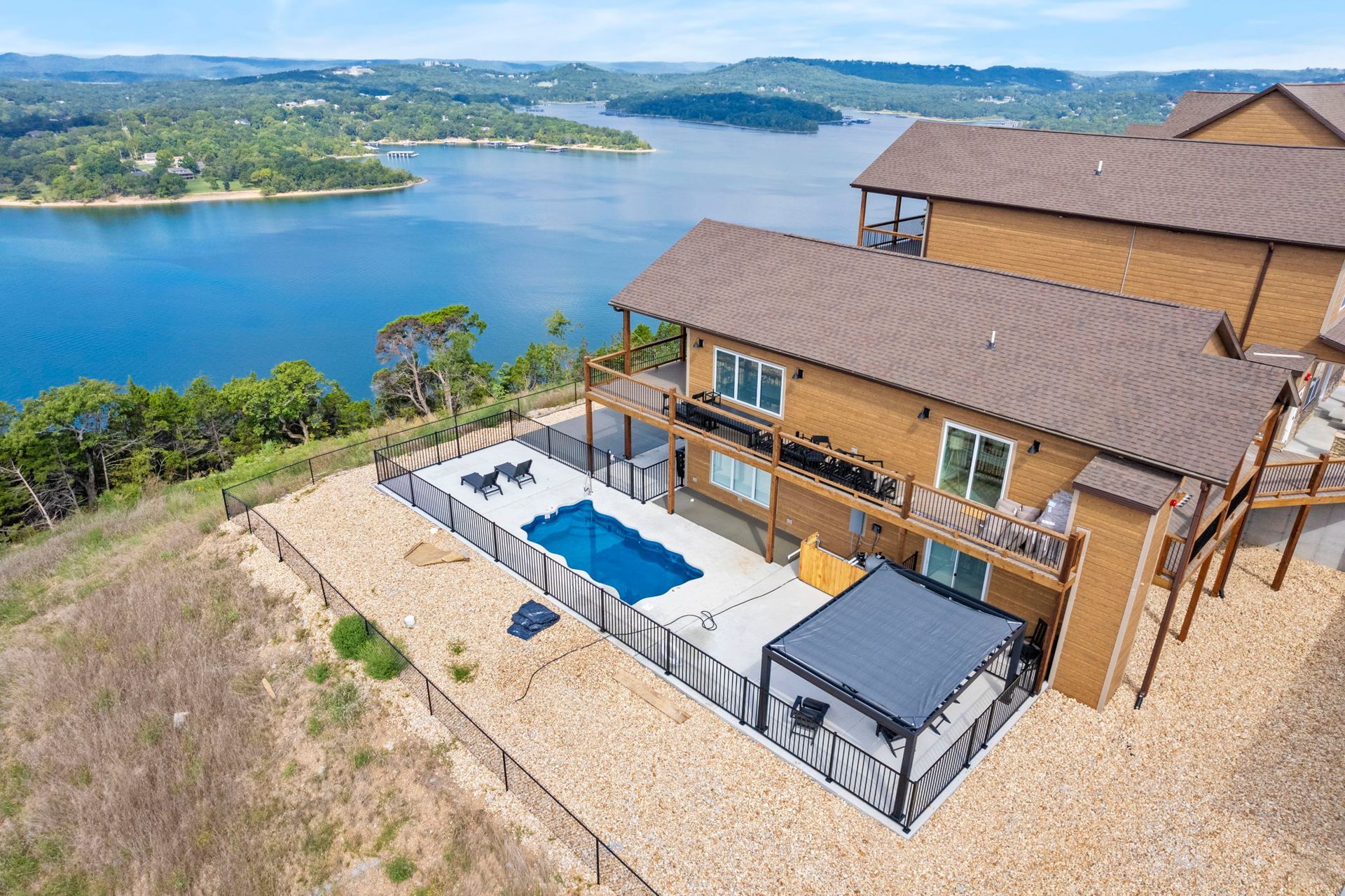 Lakefront house with pool, patio, and blue water view from a hillside