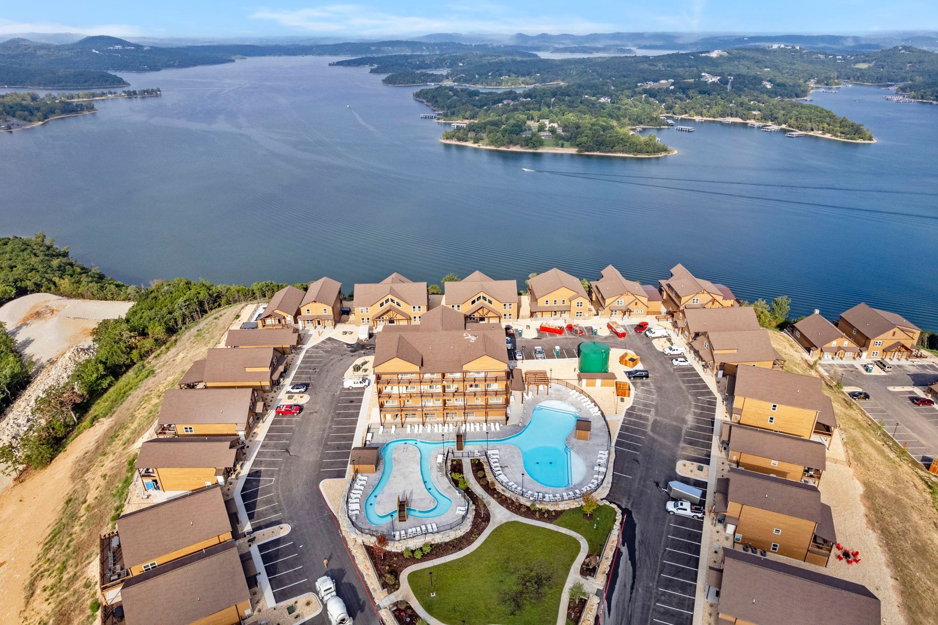 Aerial view of a lakeside resort with blue pools, tan cabins, and a large lake in the background