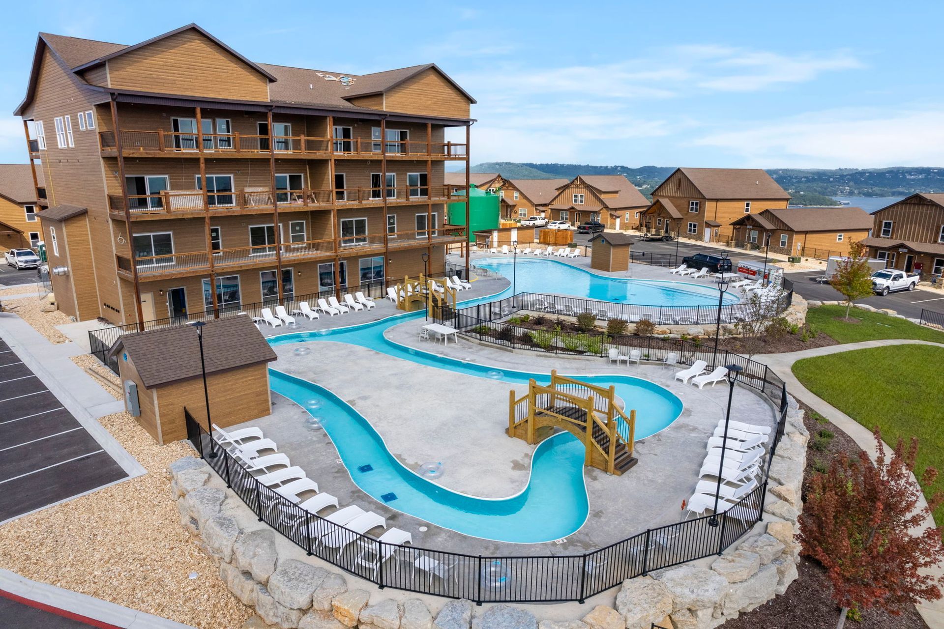 Resort pool deck with winding blue lazy river, hot tub, lounge chairs, and wooden lodge buildings