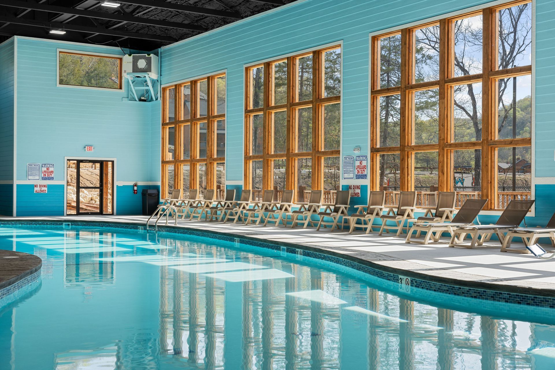 Indoor swimming pool with turquoise water, tall windows, and lounge chairs along the deck