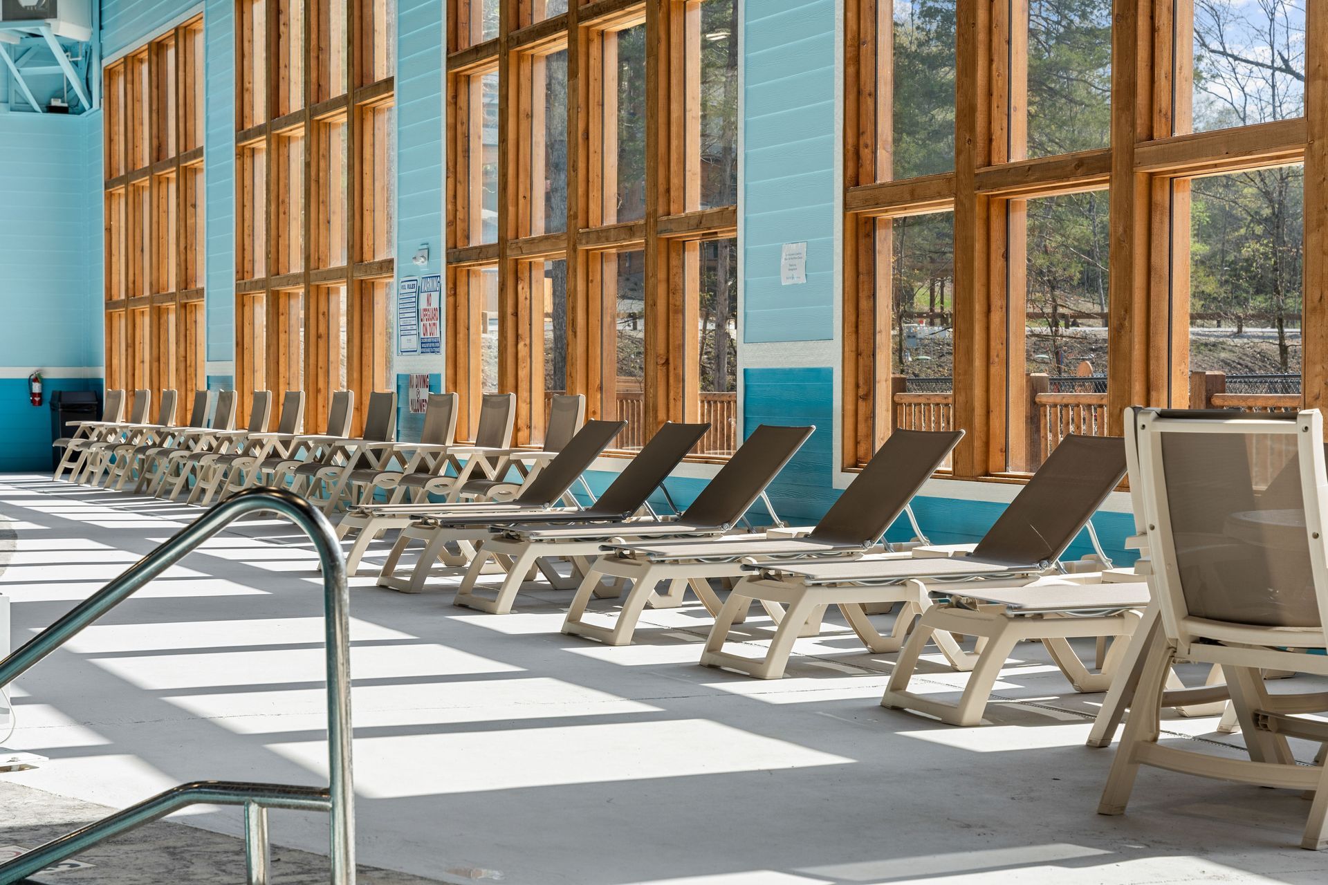 Indoor poolside lounge chairs beside tall windows in a bright, sunlit room