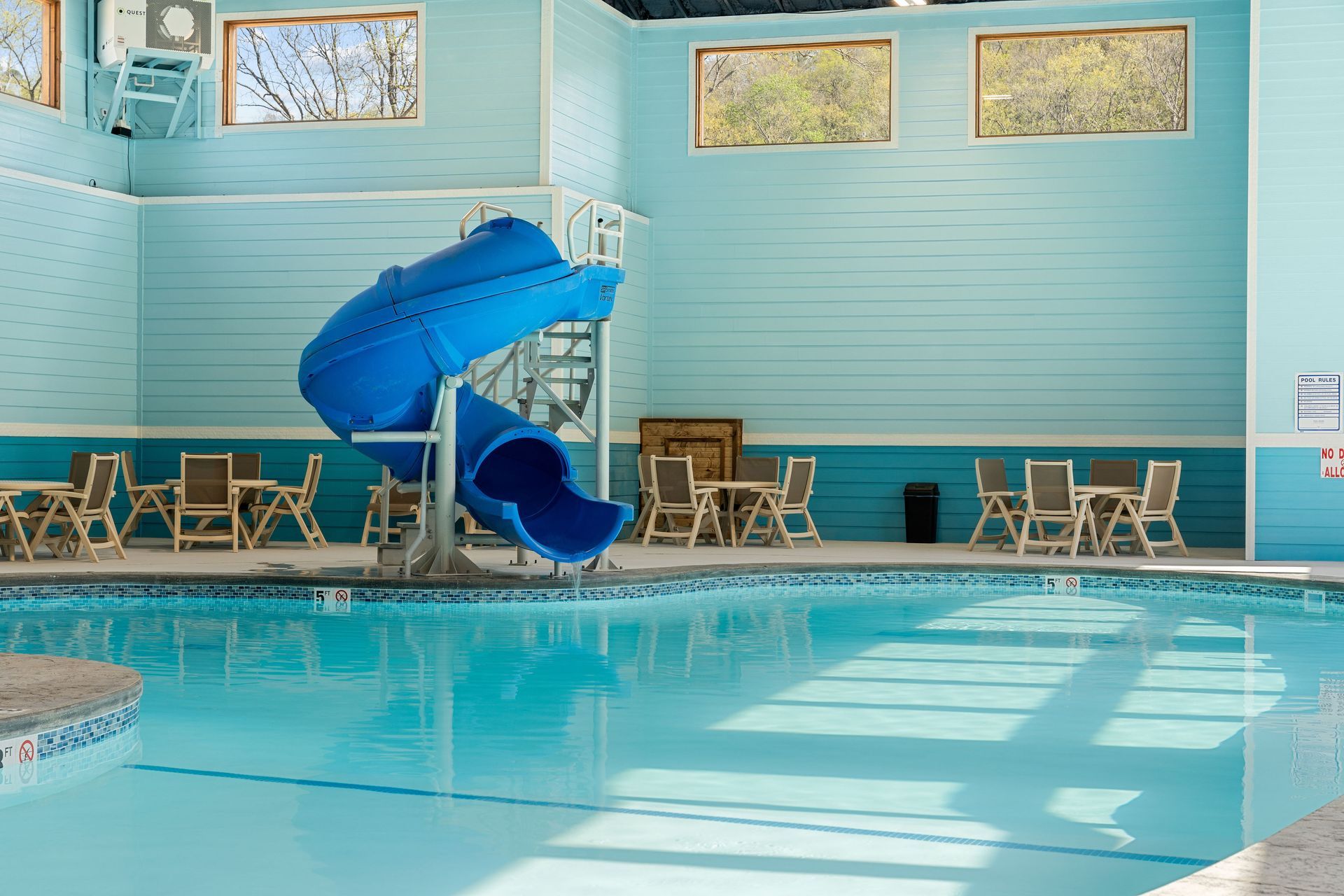 Indoor pool with a blue spiral waterslide and rows of lounge chairs along the wall