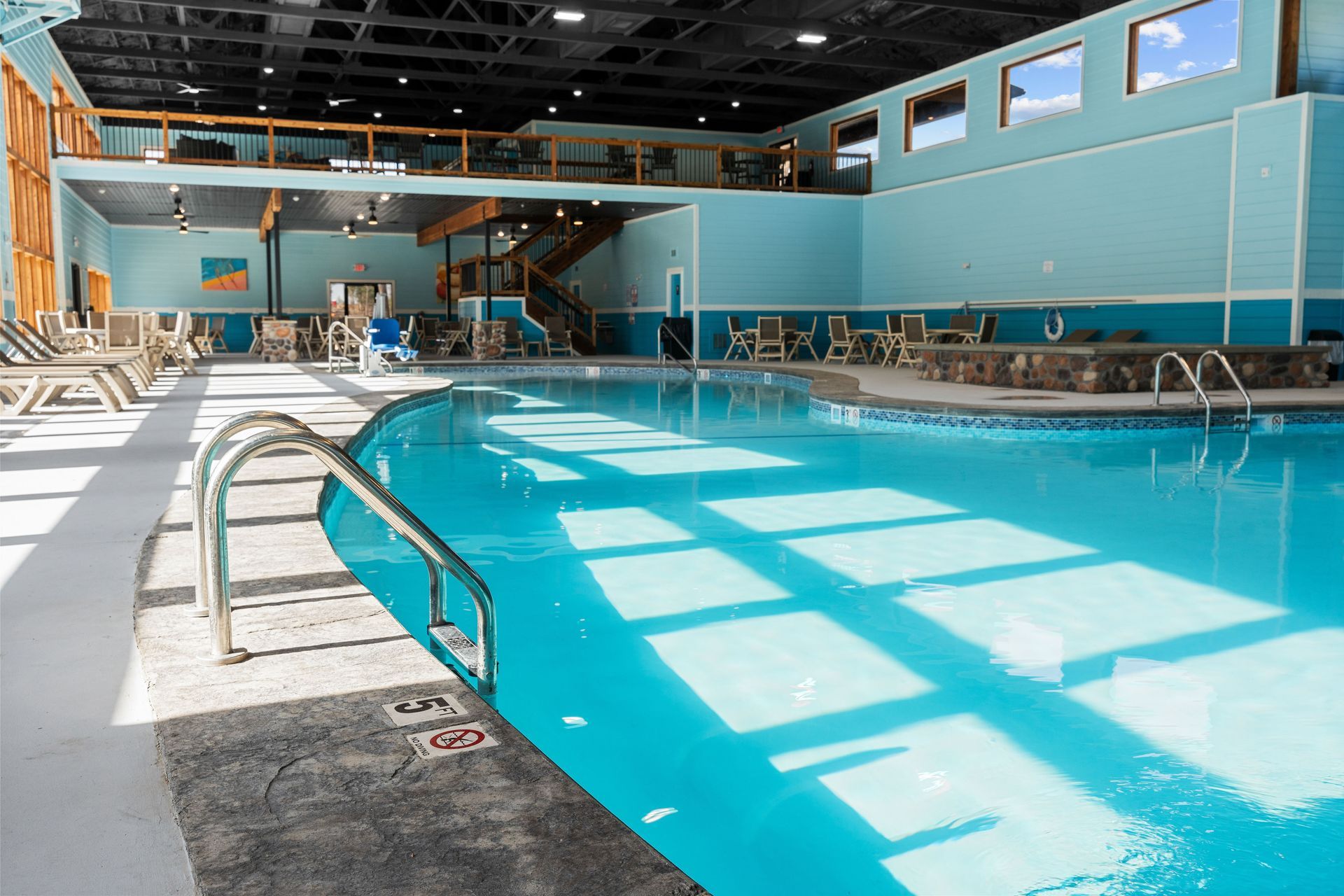Indoor swimming pool with bright blue water, lane ropes, and sunlight streaming through high windows
