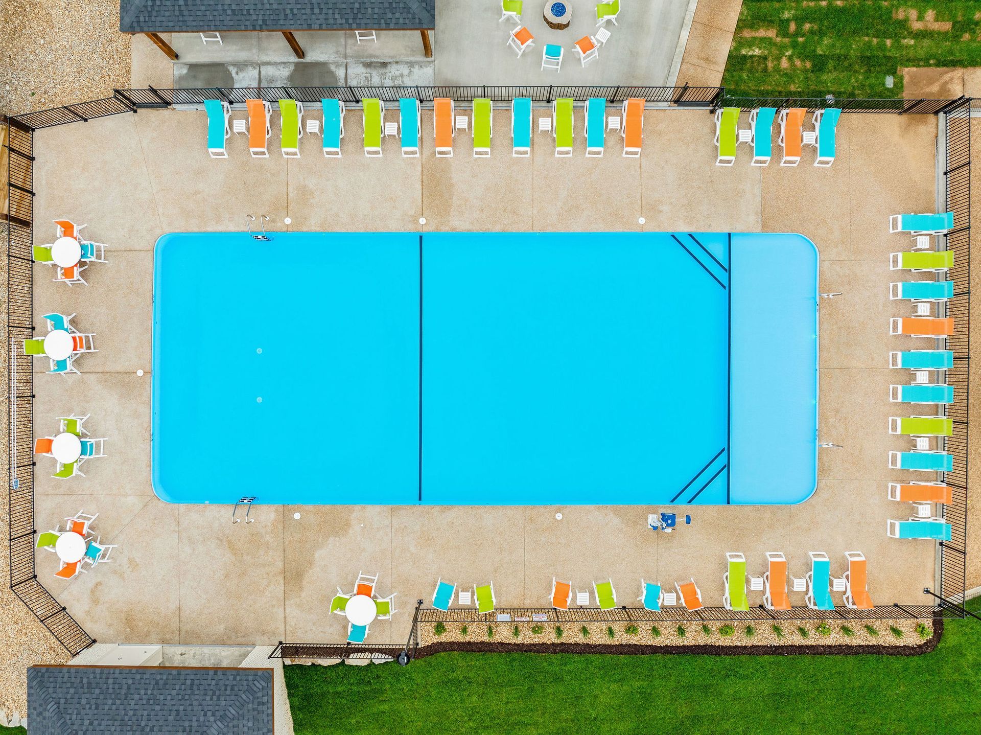 Aerial view of a rectangular swimming pool with colorful lounge chairs and tables on a patio.