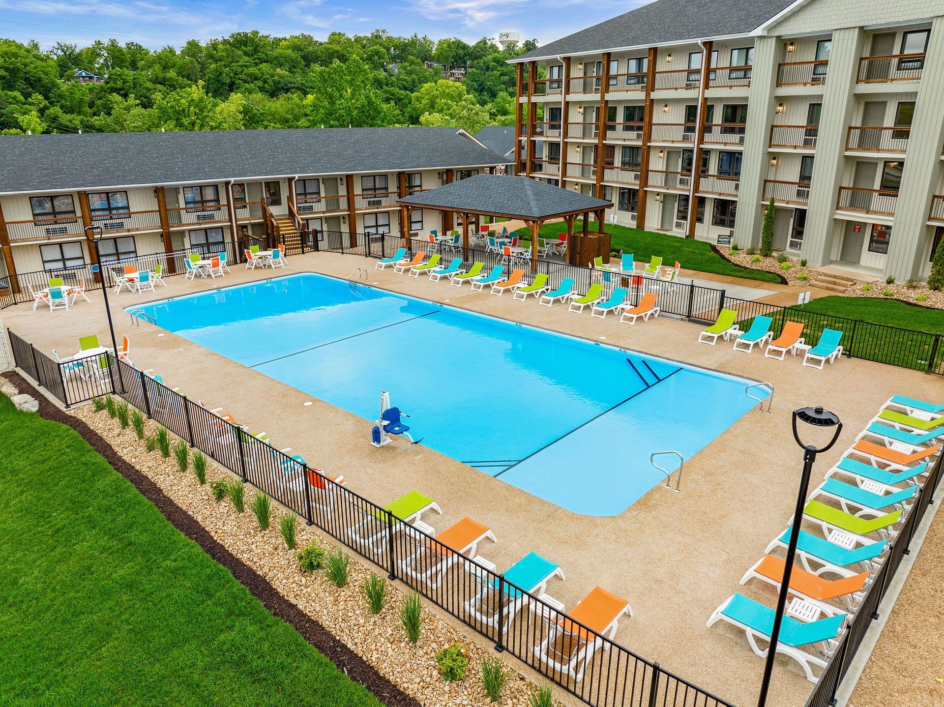 Resort pool with lounge chairs and people, surrounded by buildings and greenery