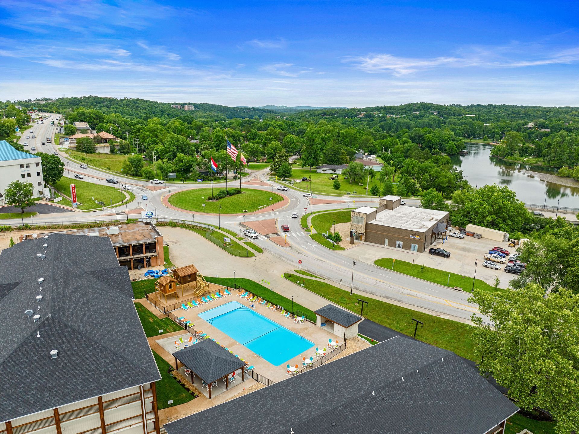 Aerial view of a resort with pools, buildings, roads, and green trees near water