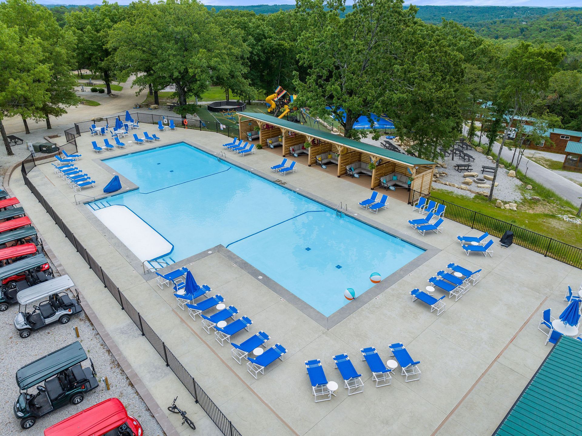 Aerial view of an outdoor swimming pool with blue lounge chairs and trees around it.