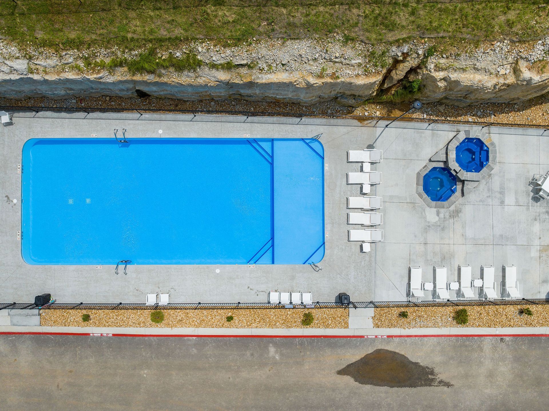 Aerial view of a blue outdoor swimming pool beside lounge chairs and two blue hot tubs.