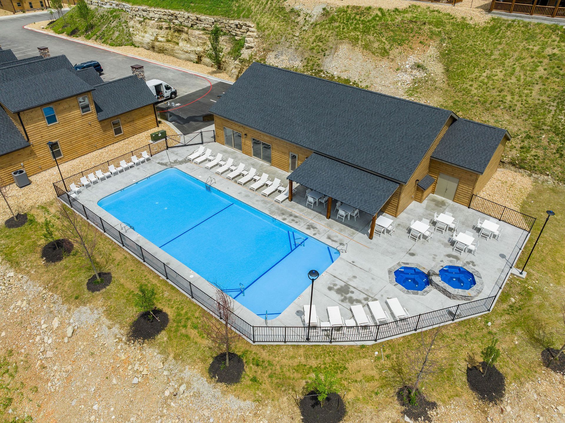 Aerial view of a lodge with a large outdoor pool and hot tubs surrounded by lounge chairs.