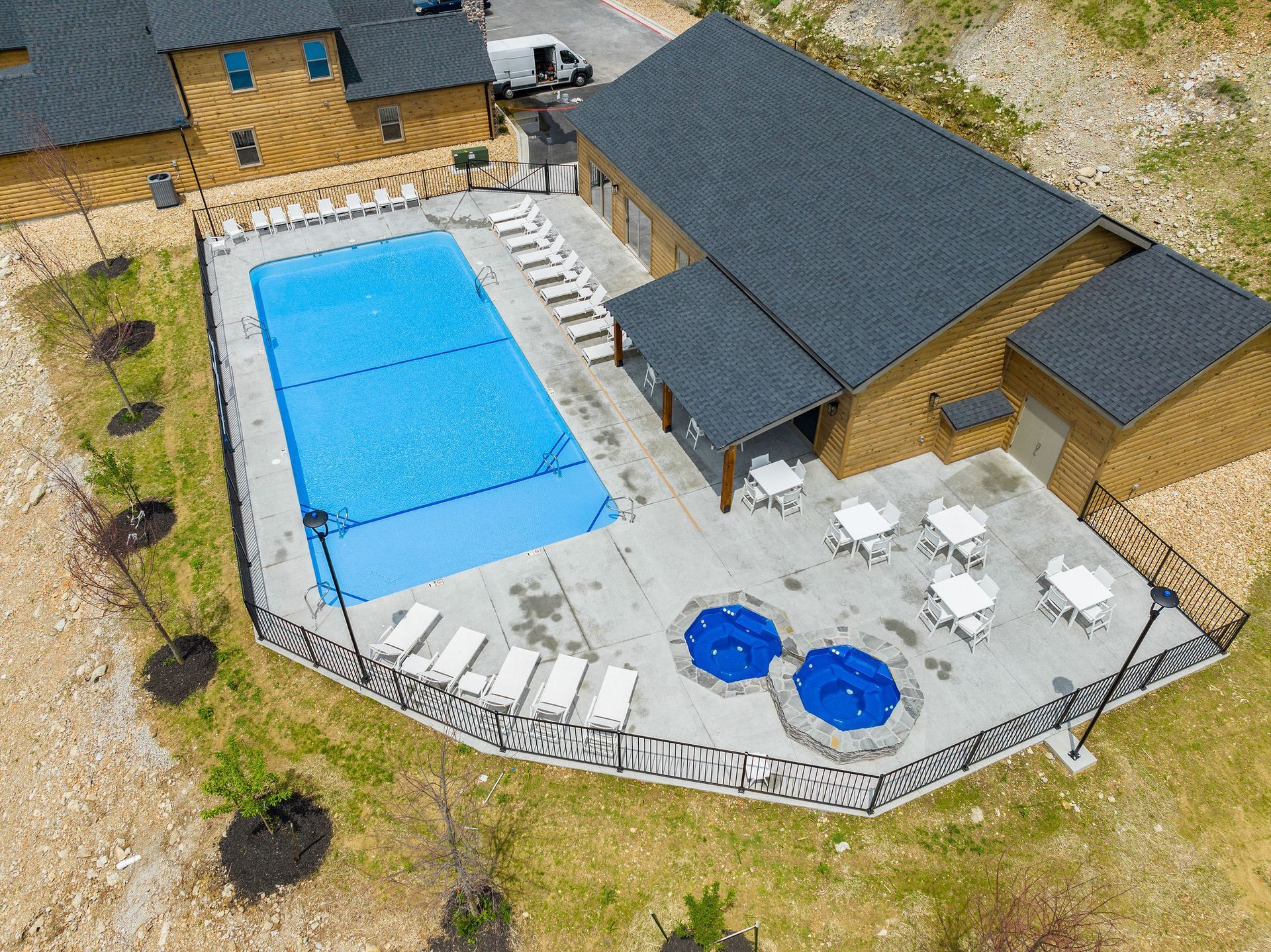 Aerial view of a lodge with a fenced patio, large blue pool, hot tubs, and lounge chairs