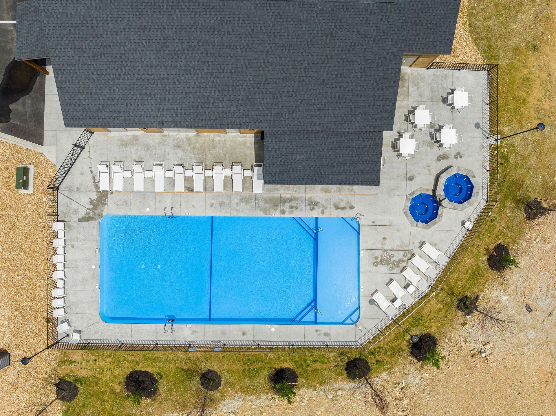 Aerial view of a backyard with a blue swimming pool, patio chairs, and umbrellas beside a house.