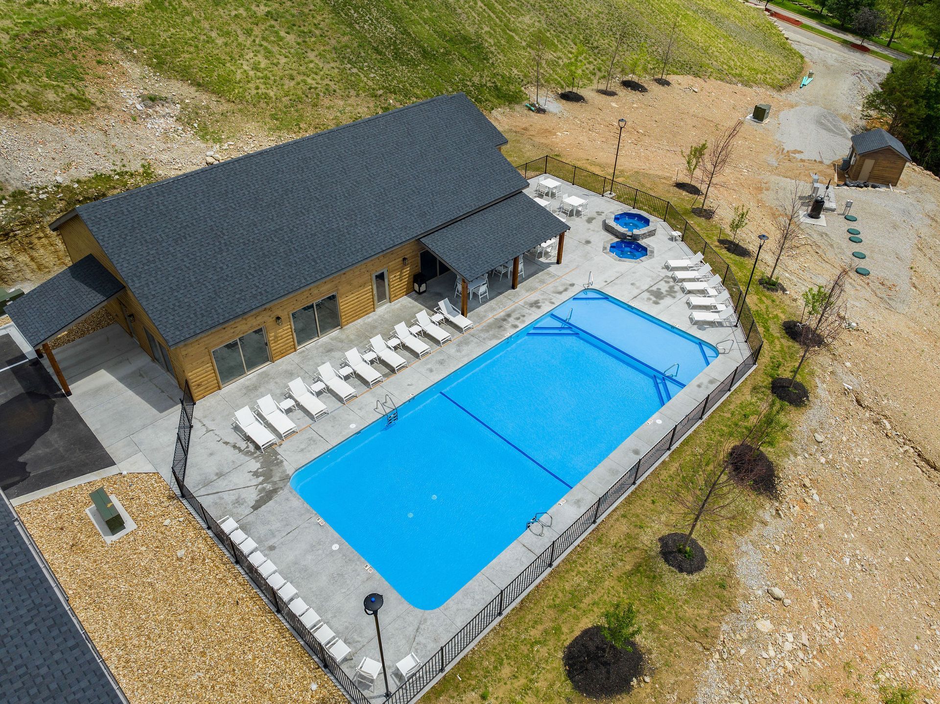Aerial view of a house with a large blue swimming pool and patio loungers in a gravel yard