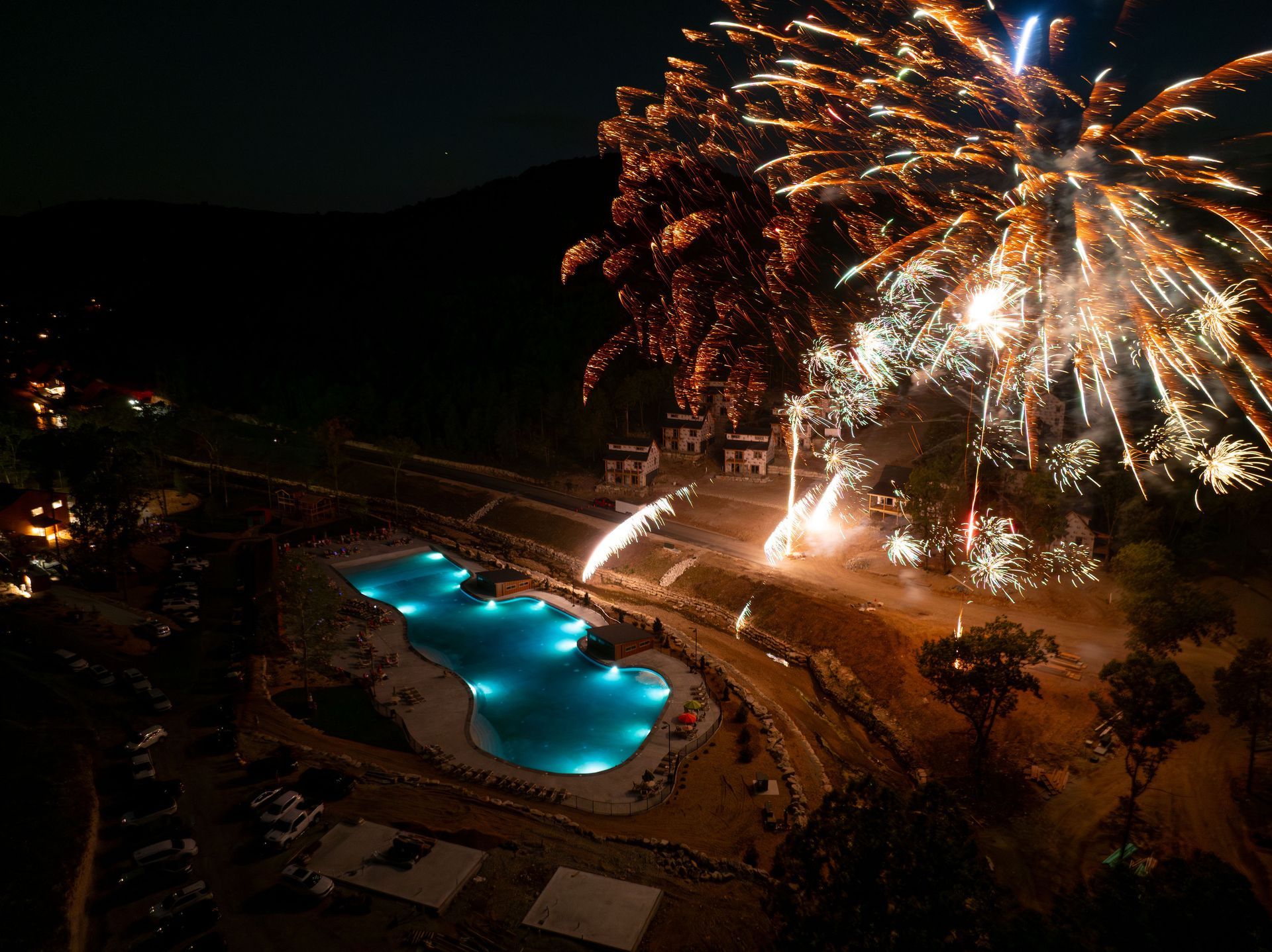 Night fireworks over a resort pool and hillside at dusk
