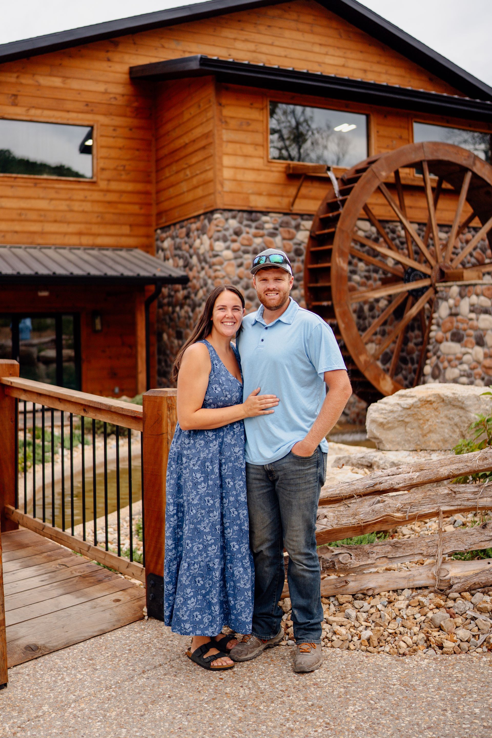 Couple standing outside a rustic wooden building with a large water wheel.
