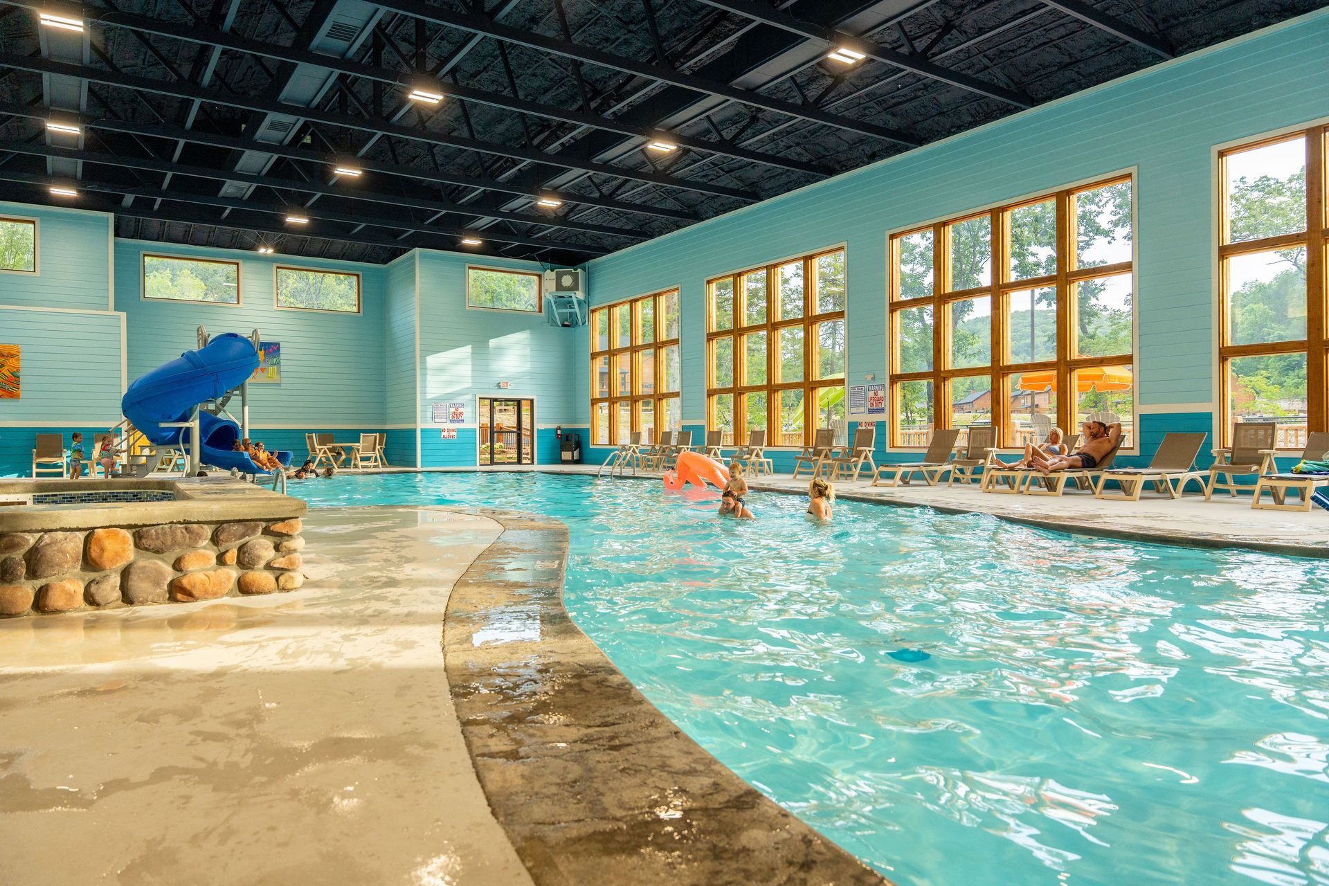 Indoor pool with turquoise water, large windows, and a person diving from the poolside.