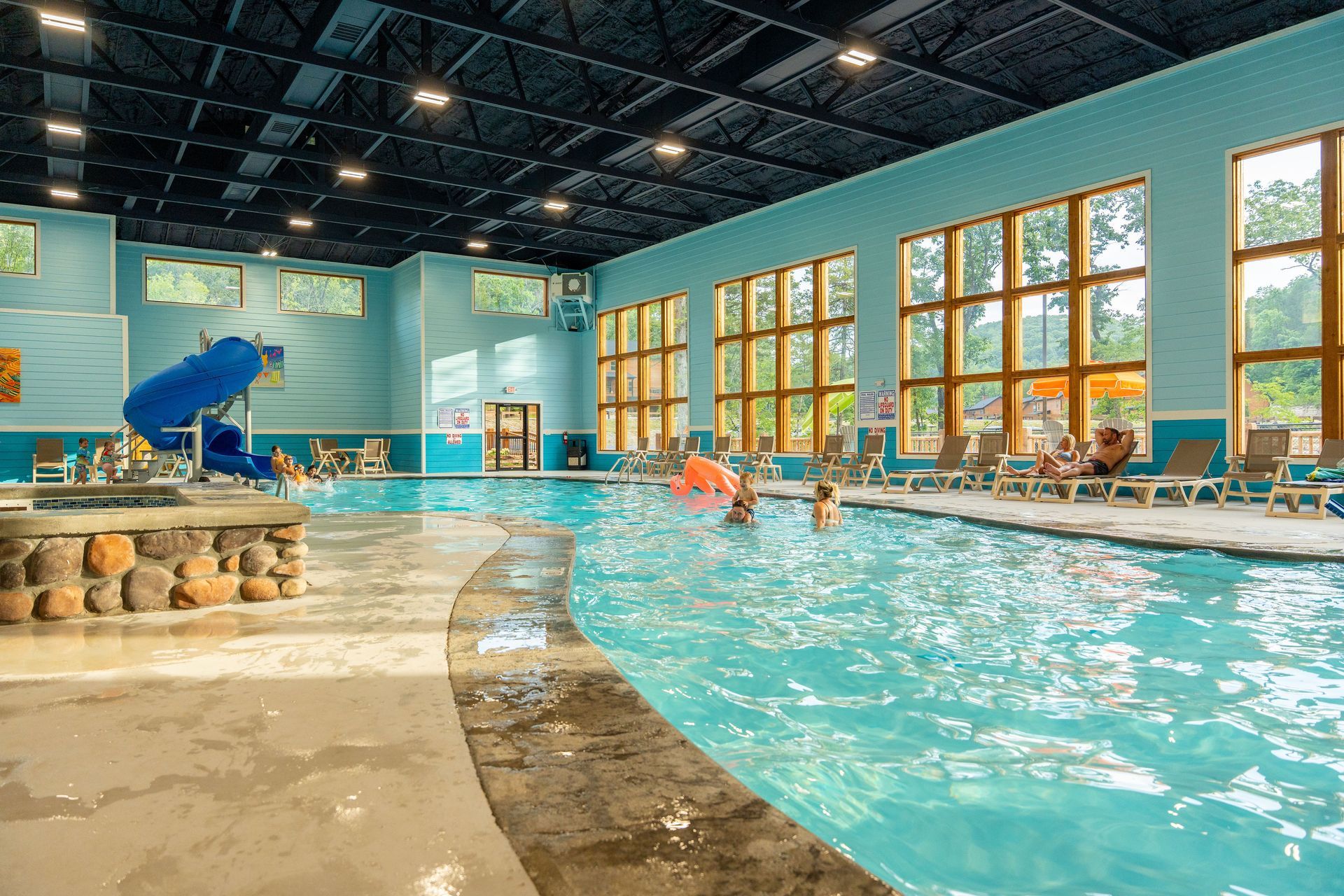 Indoor pool with swimmers, blue waterslide, and large sunlit windows