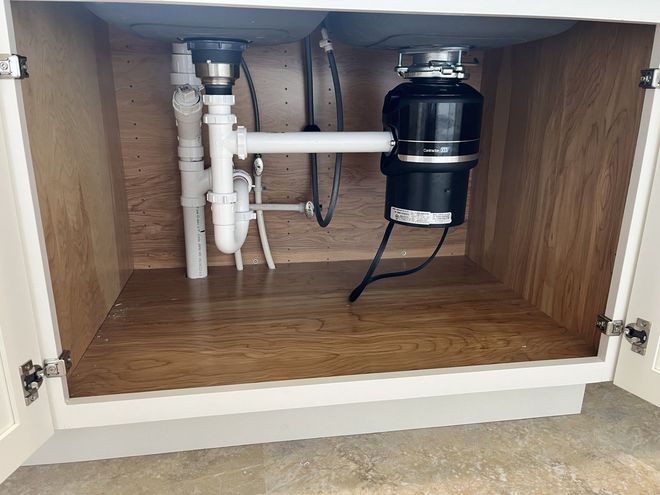 Plumber in blue overalls uses plunger on kitchen sink with tools.