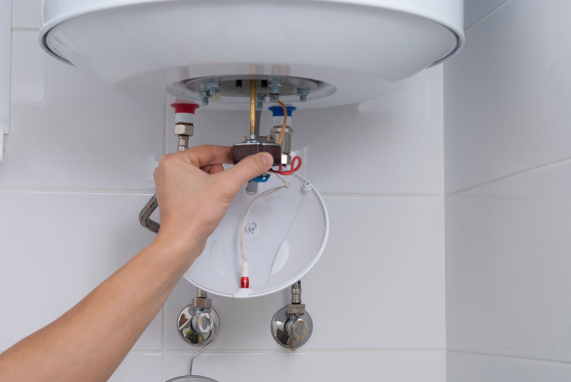 A person adjusts a control box on a white water heater, connected by pipes to the wall.