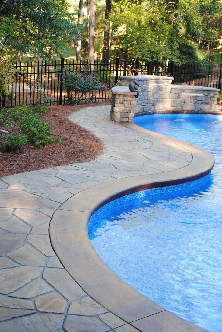 A large swimming pool with a stone walkway surrounding it.