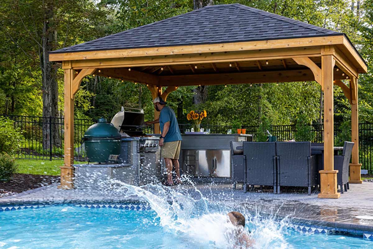A man is standing under a gazebo next to a swimming pool.