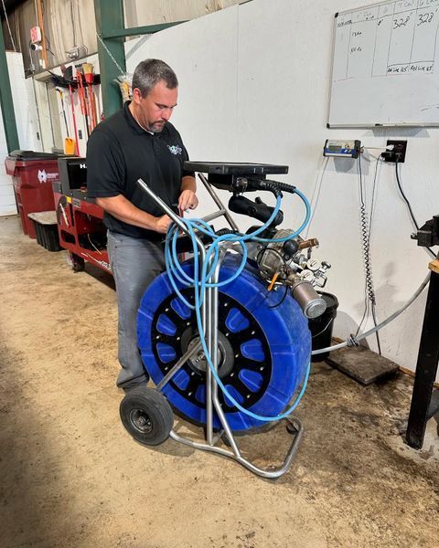 Man operating blue and silver sewer camera in a shop.