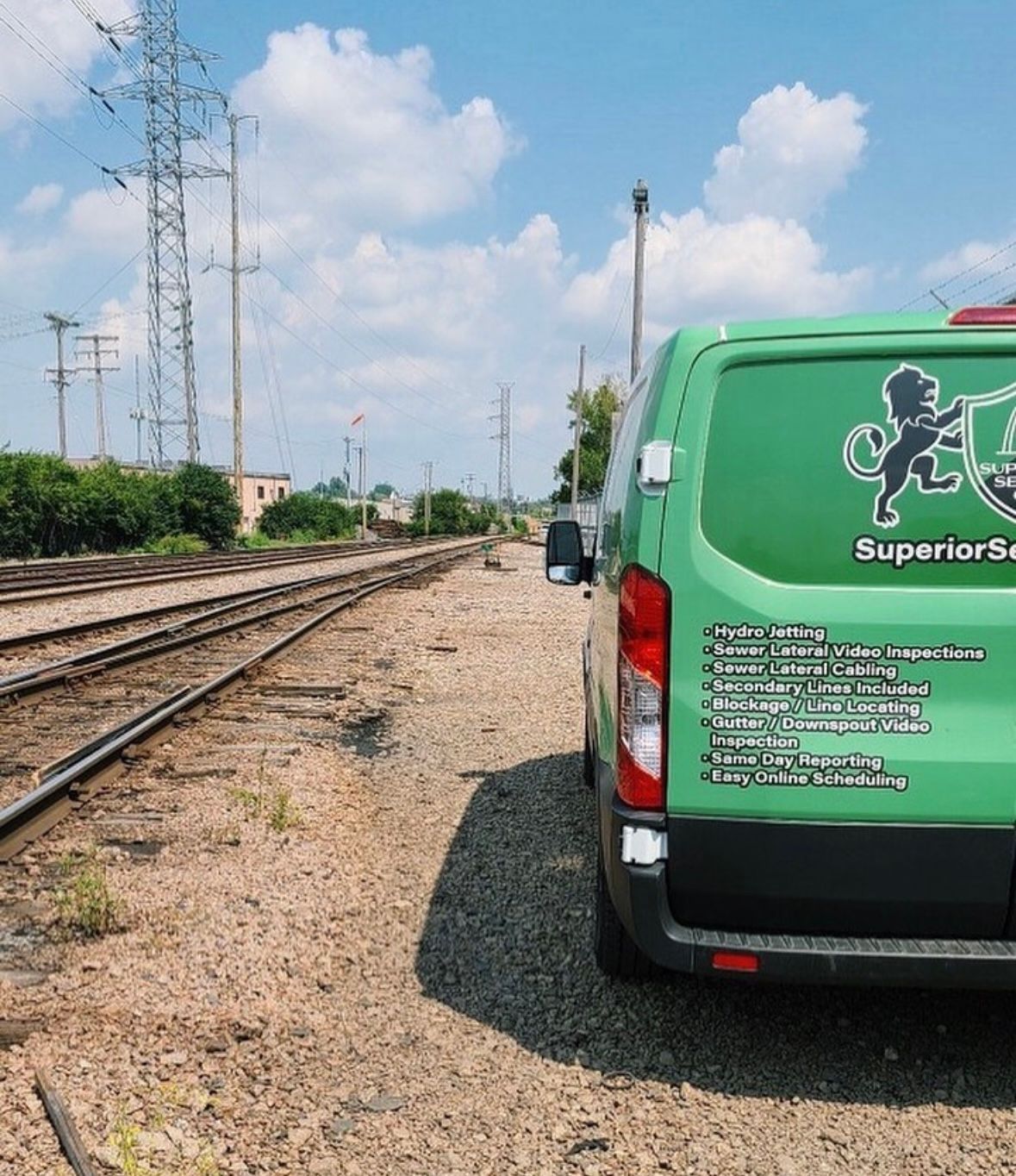 Green van with Superior Service logo parked beside train tracks under a blue sky.