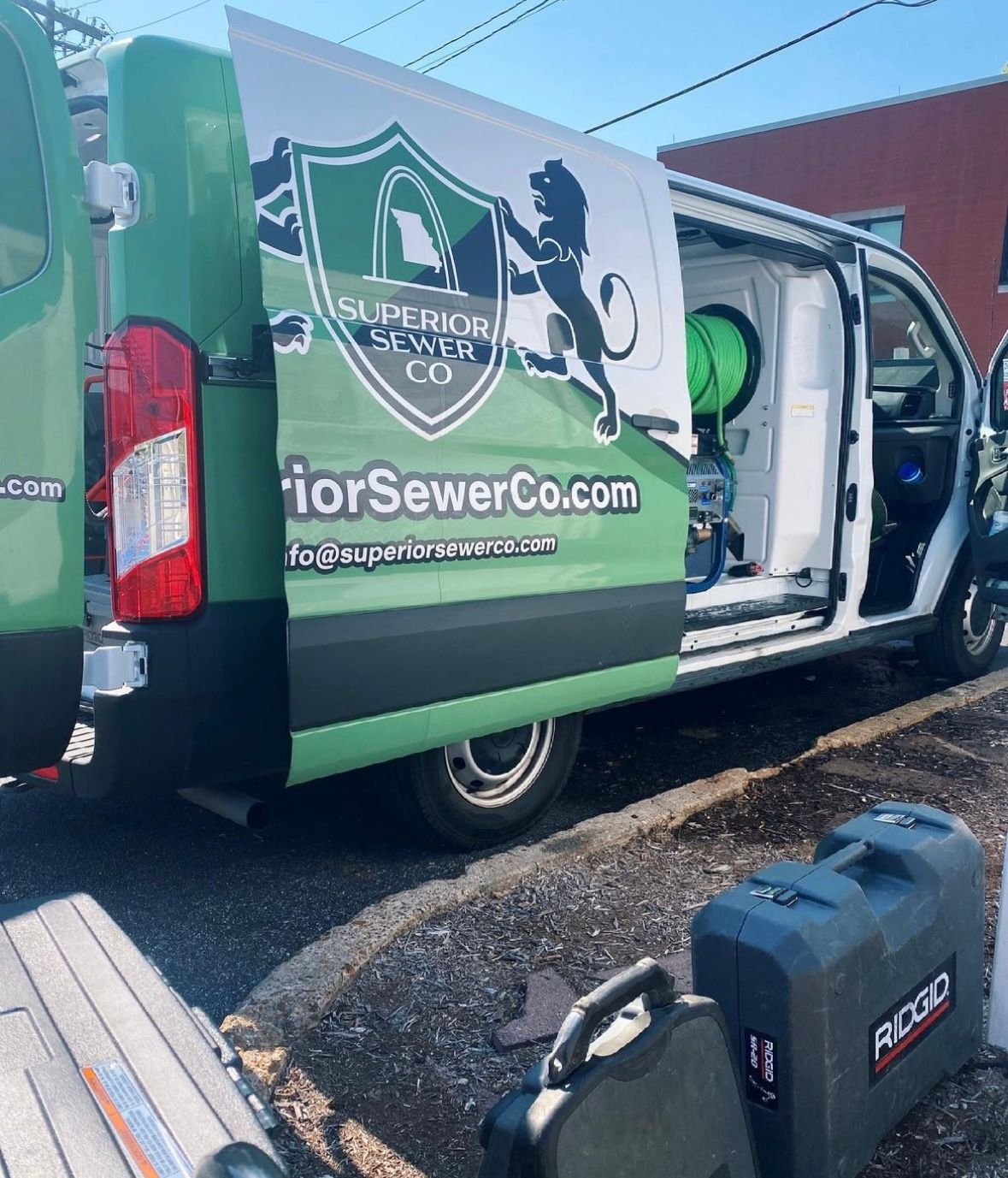 Green and white Superior Sewer Co. van with open doors, tools on the ground.