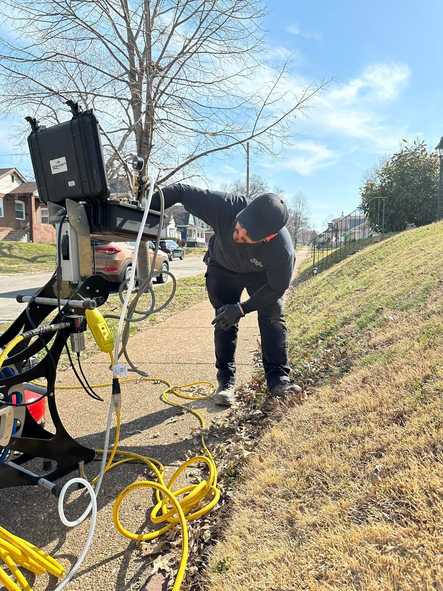 Person in dark clothing working on equipment outdoors on a sunny day.