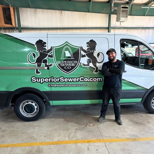 Man stands by Superior Sewer Co. van; green and white logo with lions, website address.