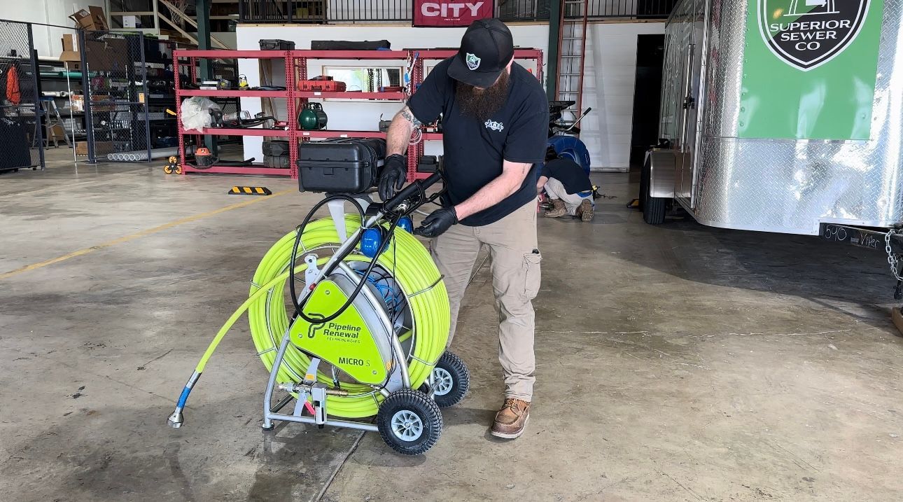 Man working on a sewer inspection camera on a rolling cart in a garage.
