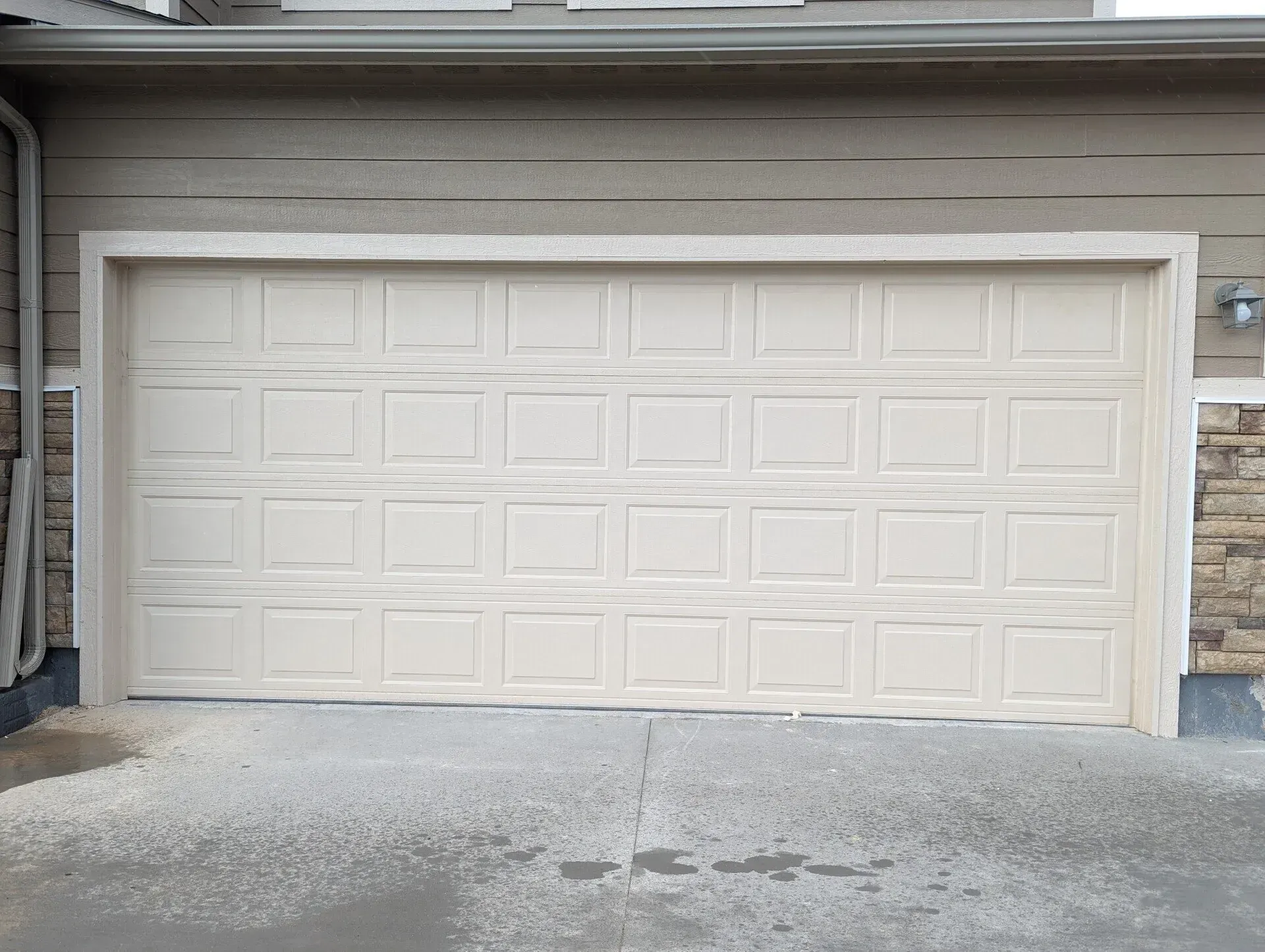 Beige garage door on a light tan house with stone siding. Concrete driveway.