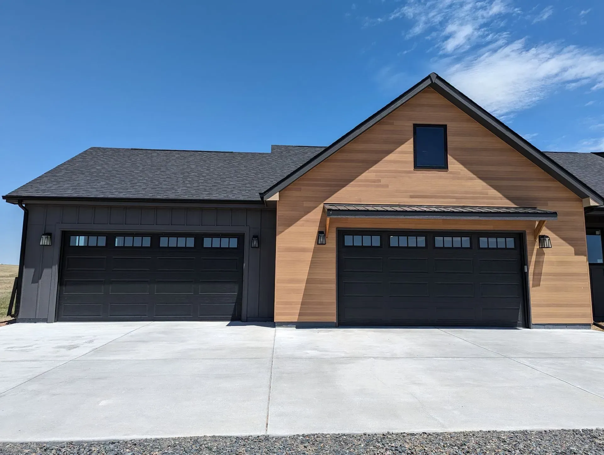 Two-car garage with black doors and light brown wood siding under a blue sky.