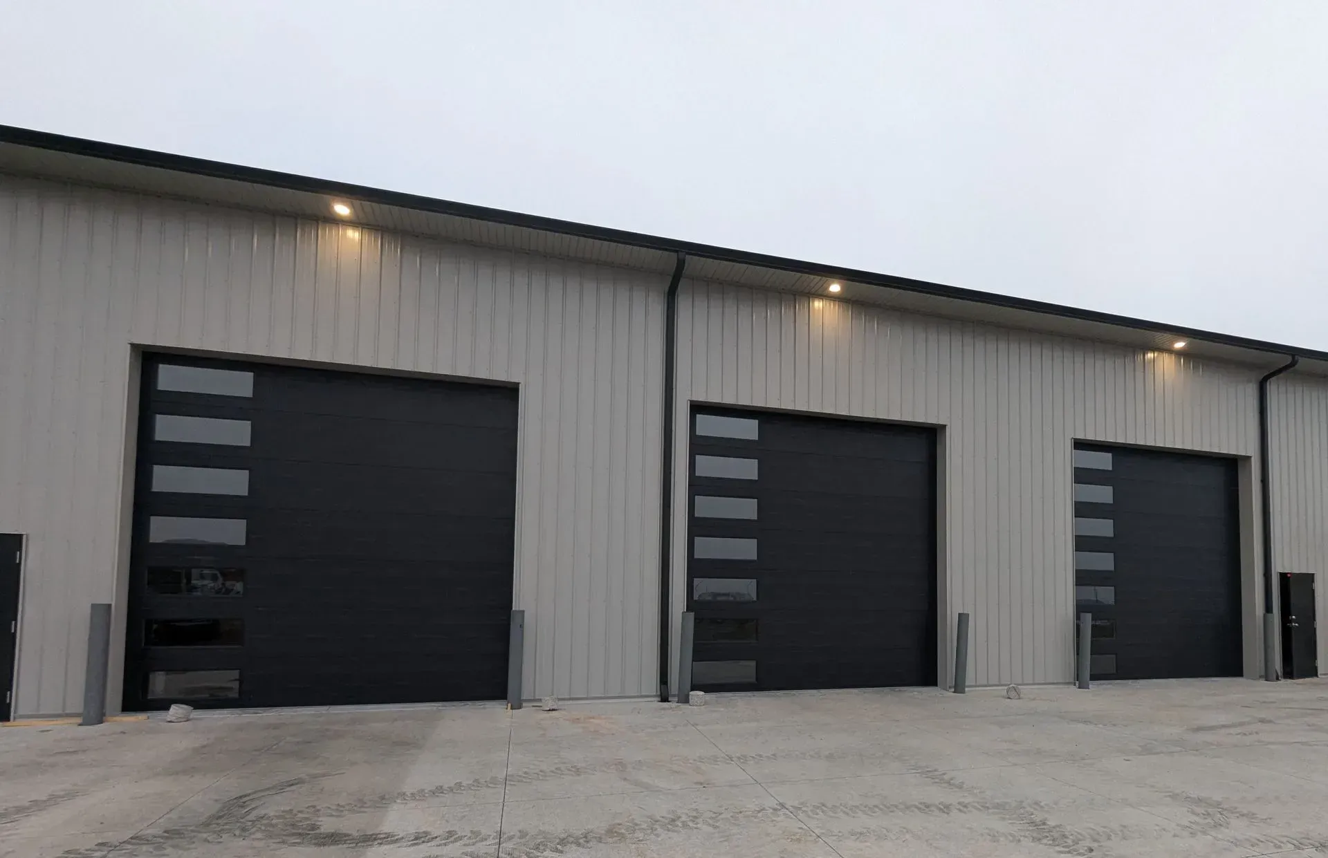 Three black garage doors with glass panels on a light-colored industrial building.