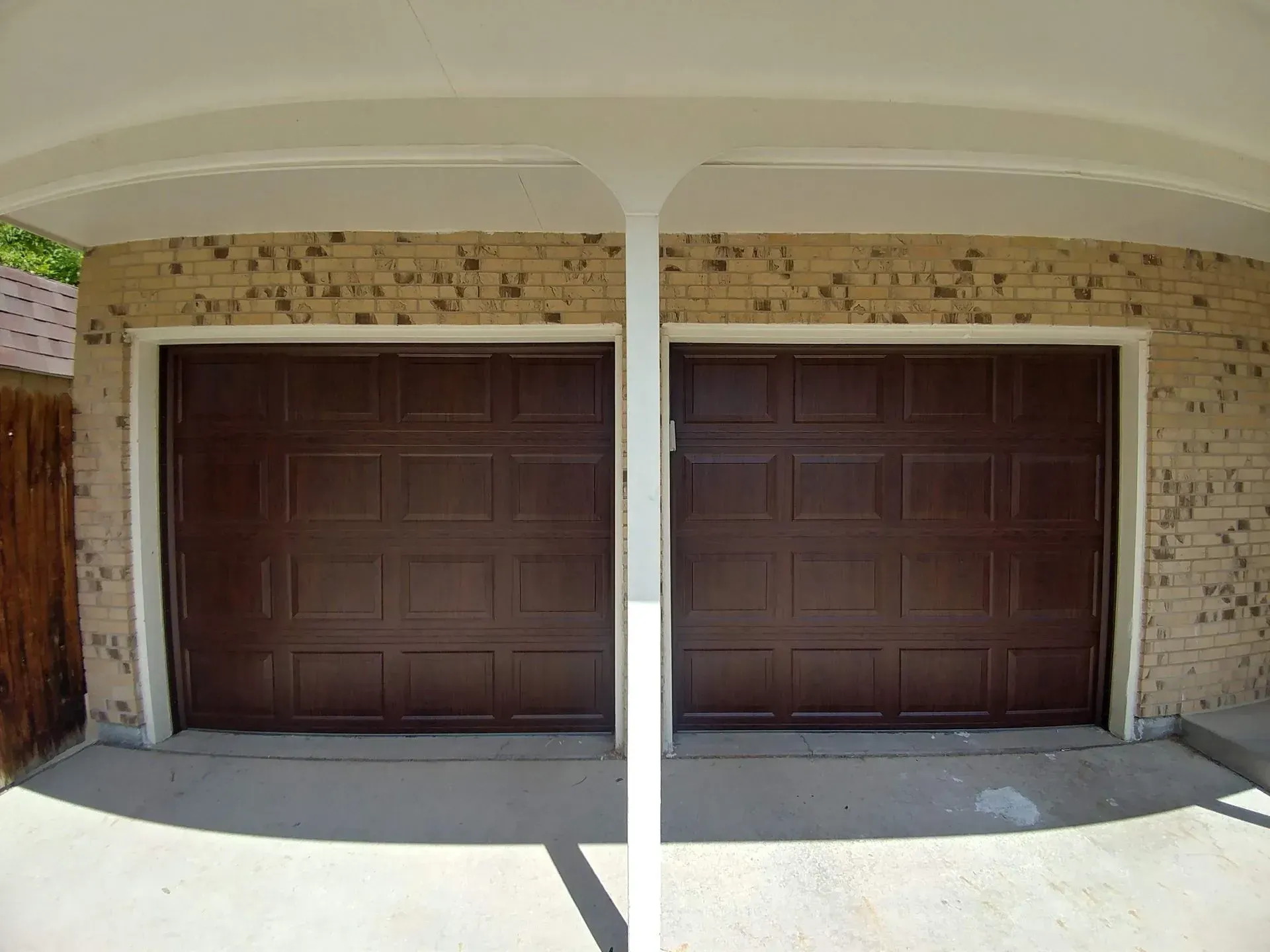 Two dark brown garage doors under a white covered structure, on a brick wall.