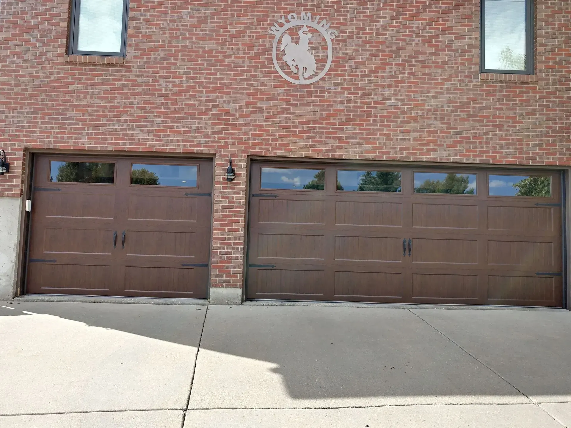 Two brown garage doors on a brick building with a logo above the larger door.