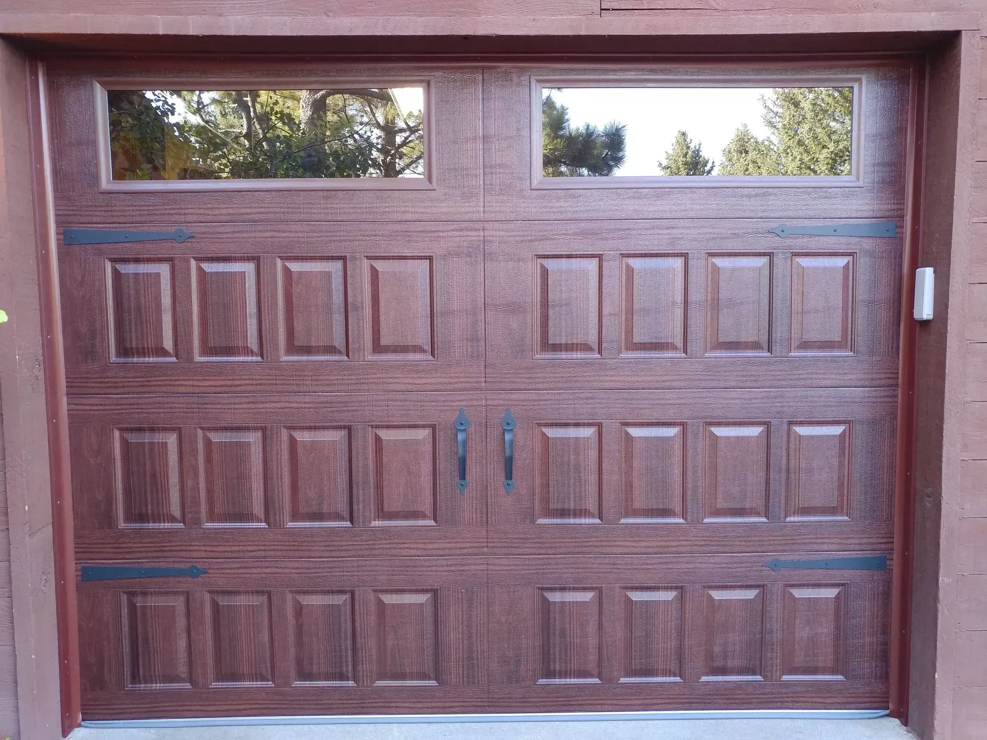 Brown garage door with two rectangular windows, decorative hardware, and wood-grain texture.