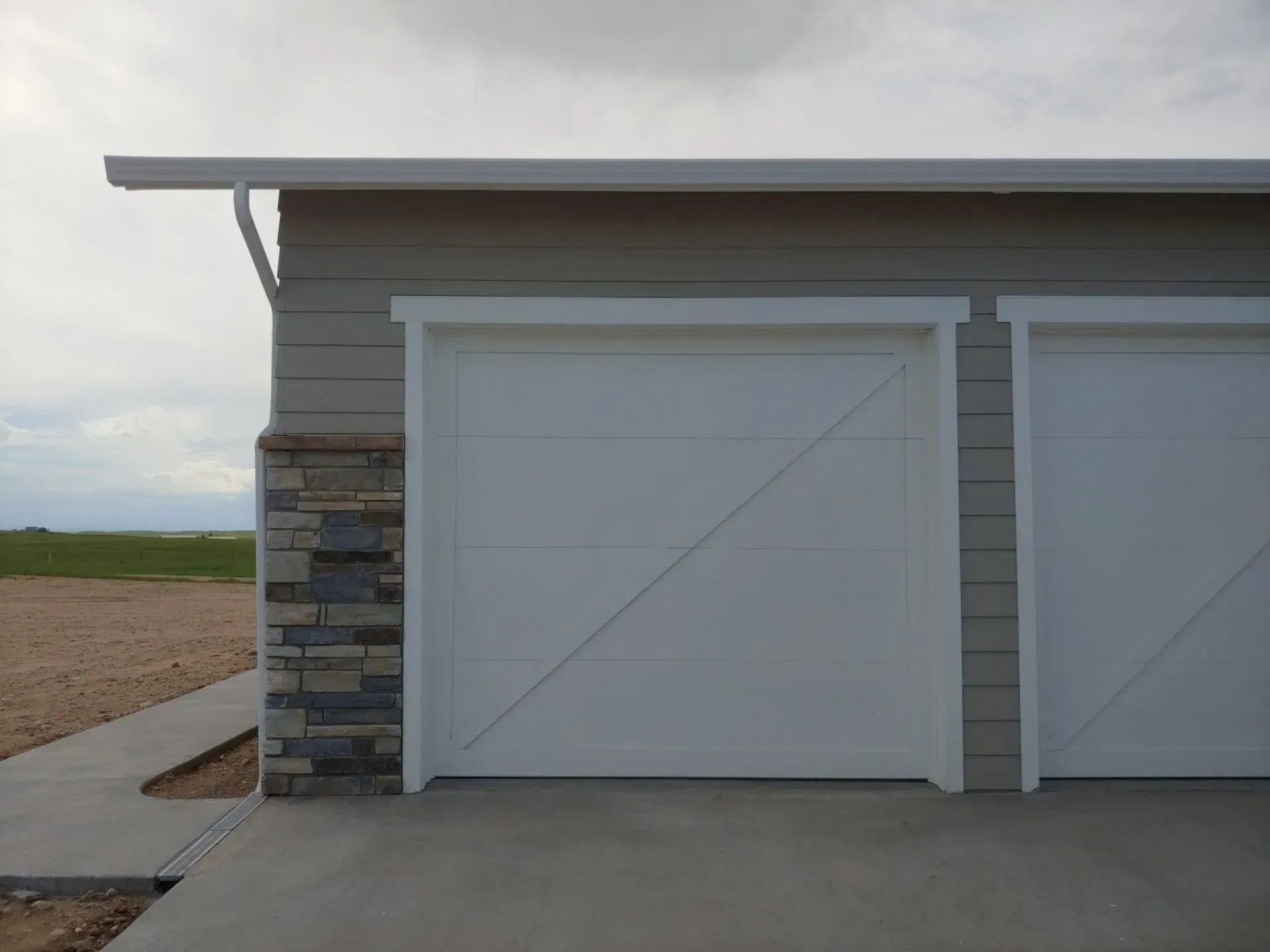 White garage doors with diagonal design on a gray building with stone accents. Concrete driveway.