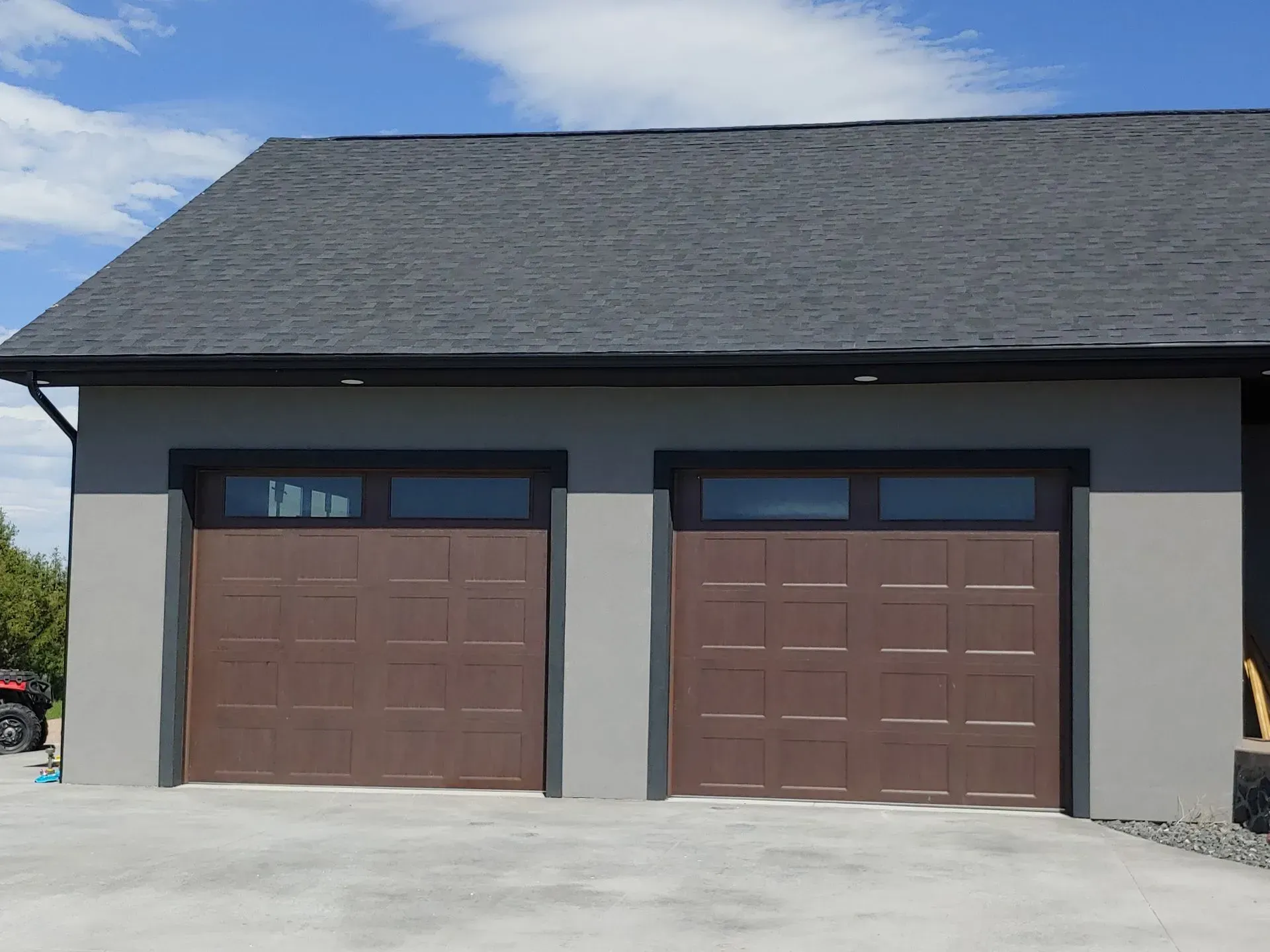 Brown garage doors with windows on a gray building, black roof, and concrete driveway.