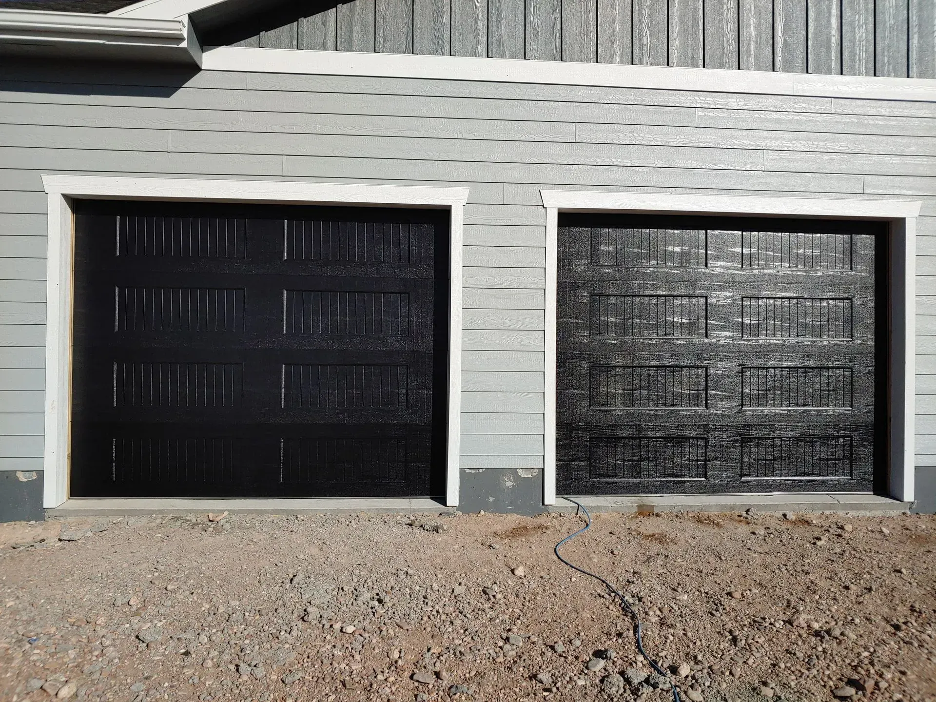 Two black garage doors with white trim in a gray building.